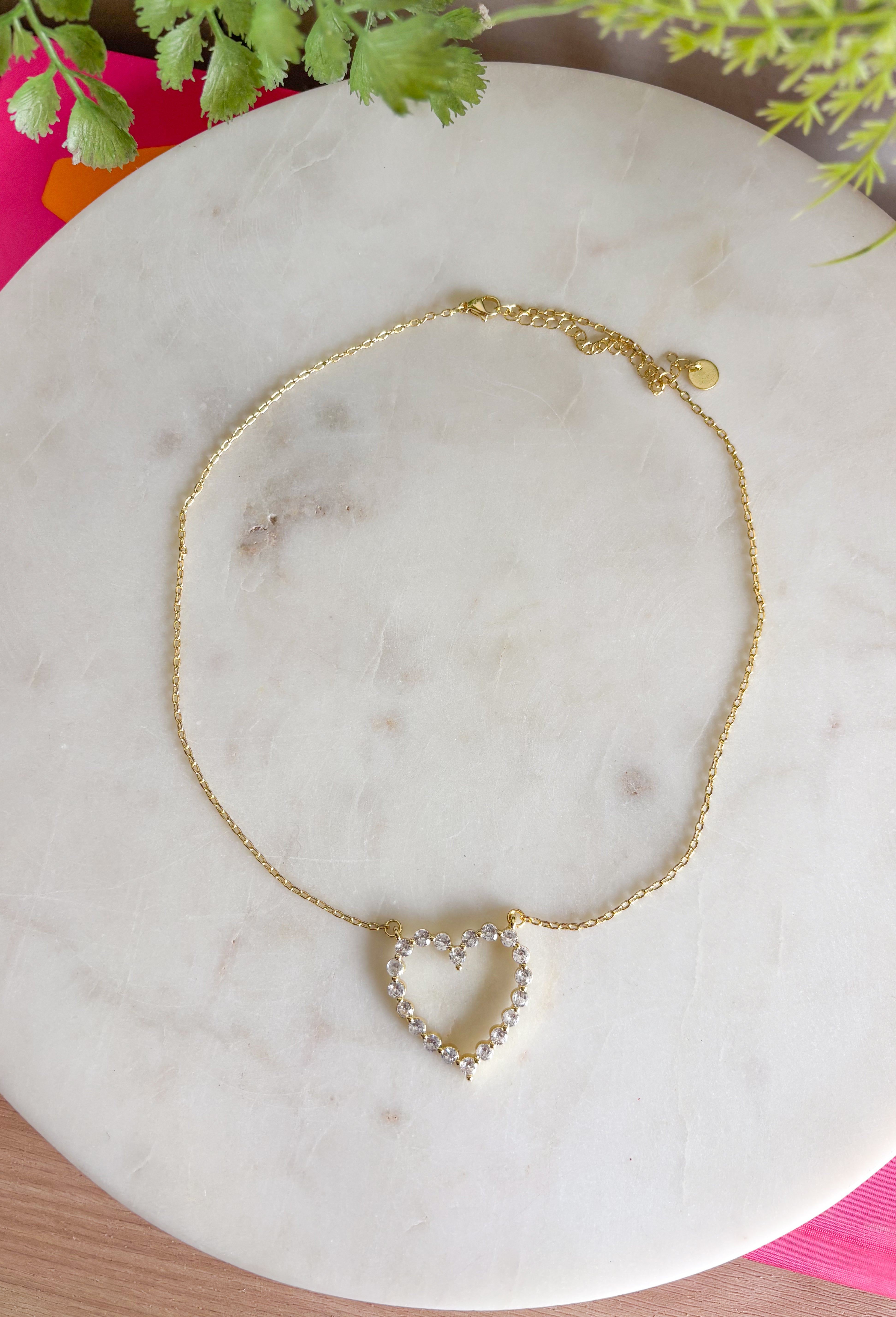 A sweet little sparkle you’ll reach for again and again! This delicate gold necklace features an open heart pendant adorned with shimmering crystal details that catch the light beautifully. The simple yet meaningful design makes it a timeless piece that adds a touch of shine to any outfit. Set on a fine gold chain with an adjustable length, it’s perfect for wearing on its own or layering with your favorite necklaces. 