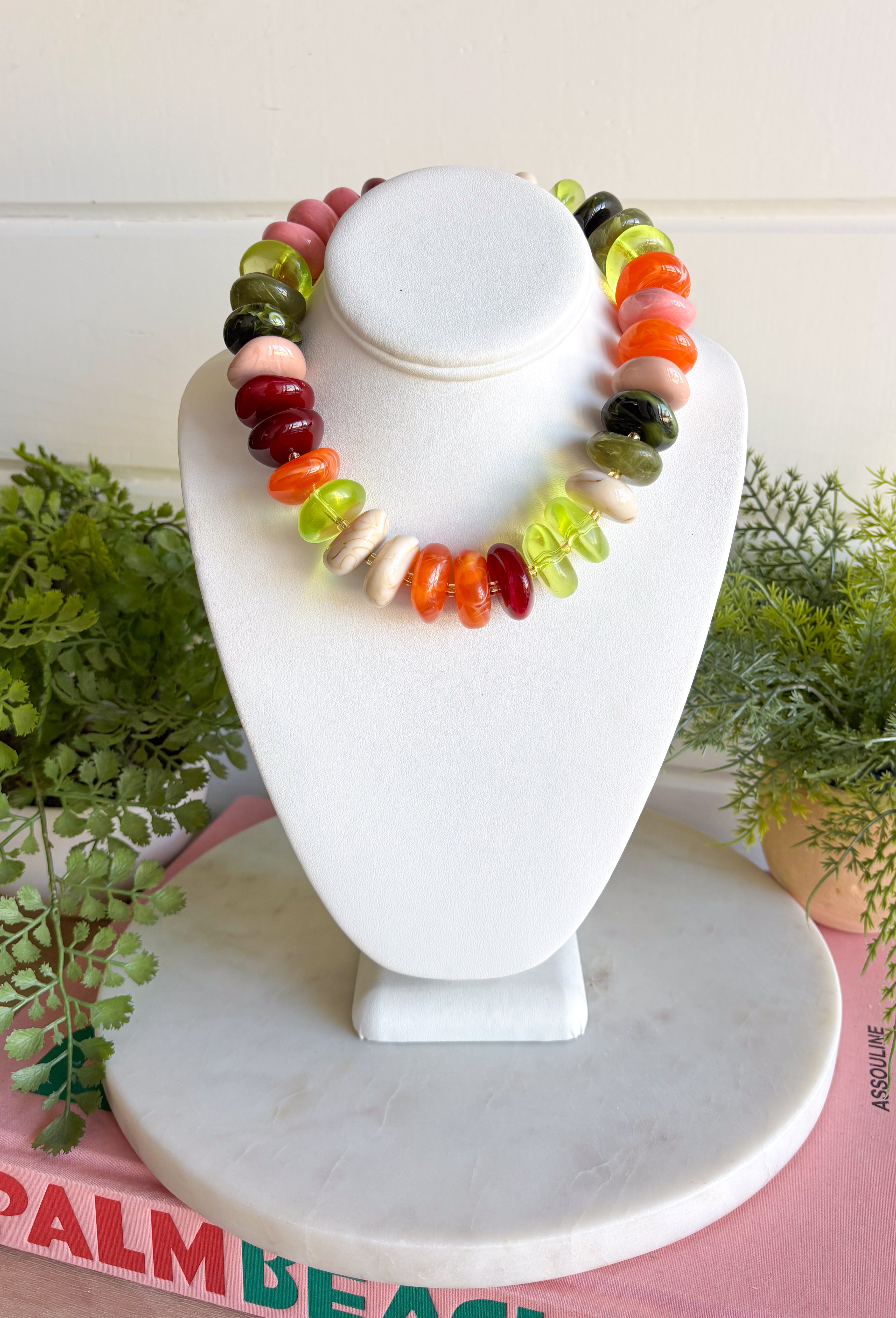 A multicolor beaded necklace displayed on a white jewelry bust