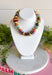 A colorful beaded necklace displayed on a white jewelry bust