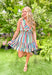 Mainstream Drama Dress, sleeveless tiered cinched waist dress with ruffing on the chest and each layer of tiering, multicolor vertical stripes cover the dress in shades of blue, yellow, green, orange, red, and white 