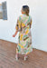 Set Me Free Midi Dress, quarter sleeve button down midi dress in a pale salmon color with sage green, amazon green and mustard yellow palm leaves printed across the dress, matching tie belt around the waist