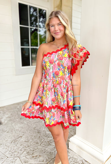 Tropical Bloom Romper, one shoulder floral print tiered romper, red rickrack hemming on each of the tiers as well as across the hem of the chest and on the ruffles of the sleeves, floral print is in the colors red, yellow, orange, green, pink, white, and blue 