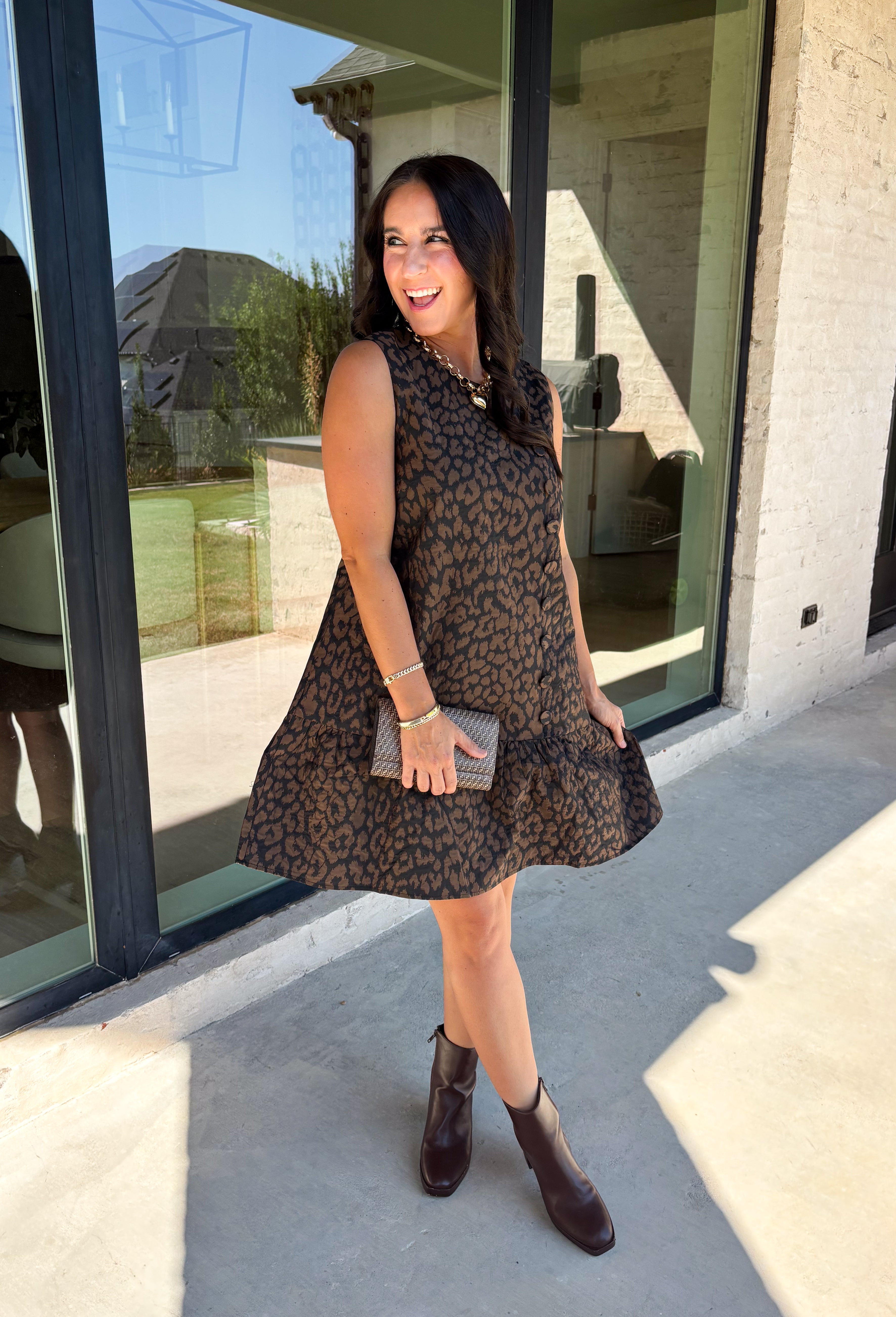 Leopard gets a refined update with this black and brown printed dress from Entro. The neutral color palette gives the statement print a classic feel, making it easy to wear for everything from dinner plans and work events to fall gatherings. A full button-down detail off centered adds an unexpected touch that sets this dress apart, while the sleeveless silhouette keeps the look clean and easy to layer. The tiered skirt adds movement and shape, and the fully lined design provides comfortable coverage.