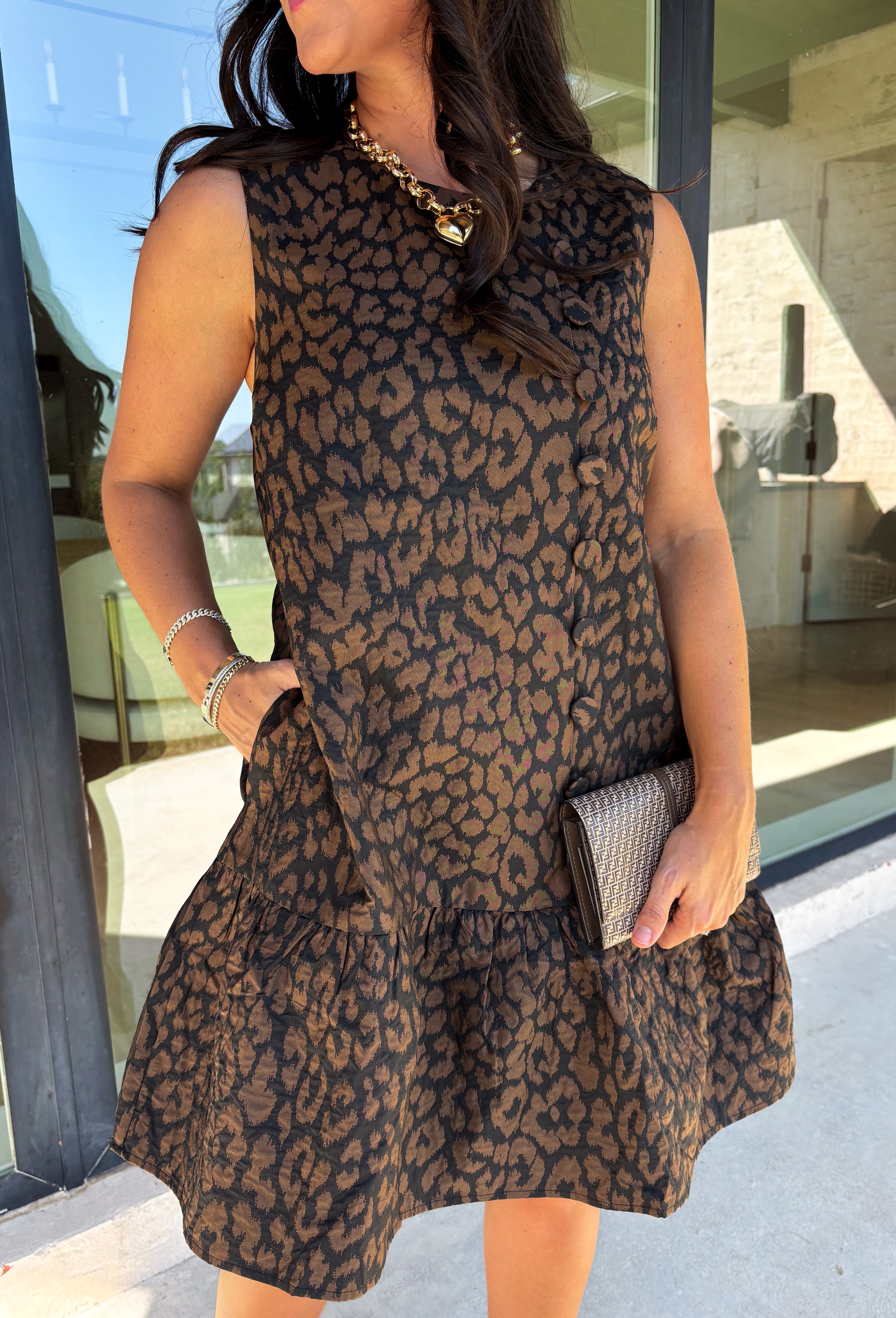 Leopard gets a refined update with this black and brown printed dress from Entro. The neutral color palette gives the statement print a classic feel, making it easy to wear for everything from dinner plans and work events to fall gatherings. A full button-down detail off centered adds an unexpected touch that sets this dress apart, while the sleeveless silhouette keeps the look clean and easy to layer. The tiered skirt adds movement and shape, and the fully lined design provides comfortable coverage.