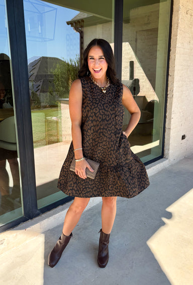 Leopard gets a refined update with this black and brown printed dress from Entro. The neutral color palette gives the statement print a classic feel, making it easy to wear for everything from dinner plans and work events to fall gatherings. A full button-down detail off centered adds an unexpected touch that sets this dress apart, while the sleeveless silhouette keeps the look clean and easy to layer. The tiered skirt adds movement and shape, and the fully lined design provides comfortable coverage.