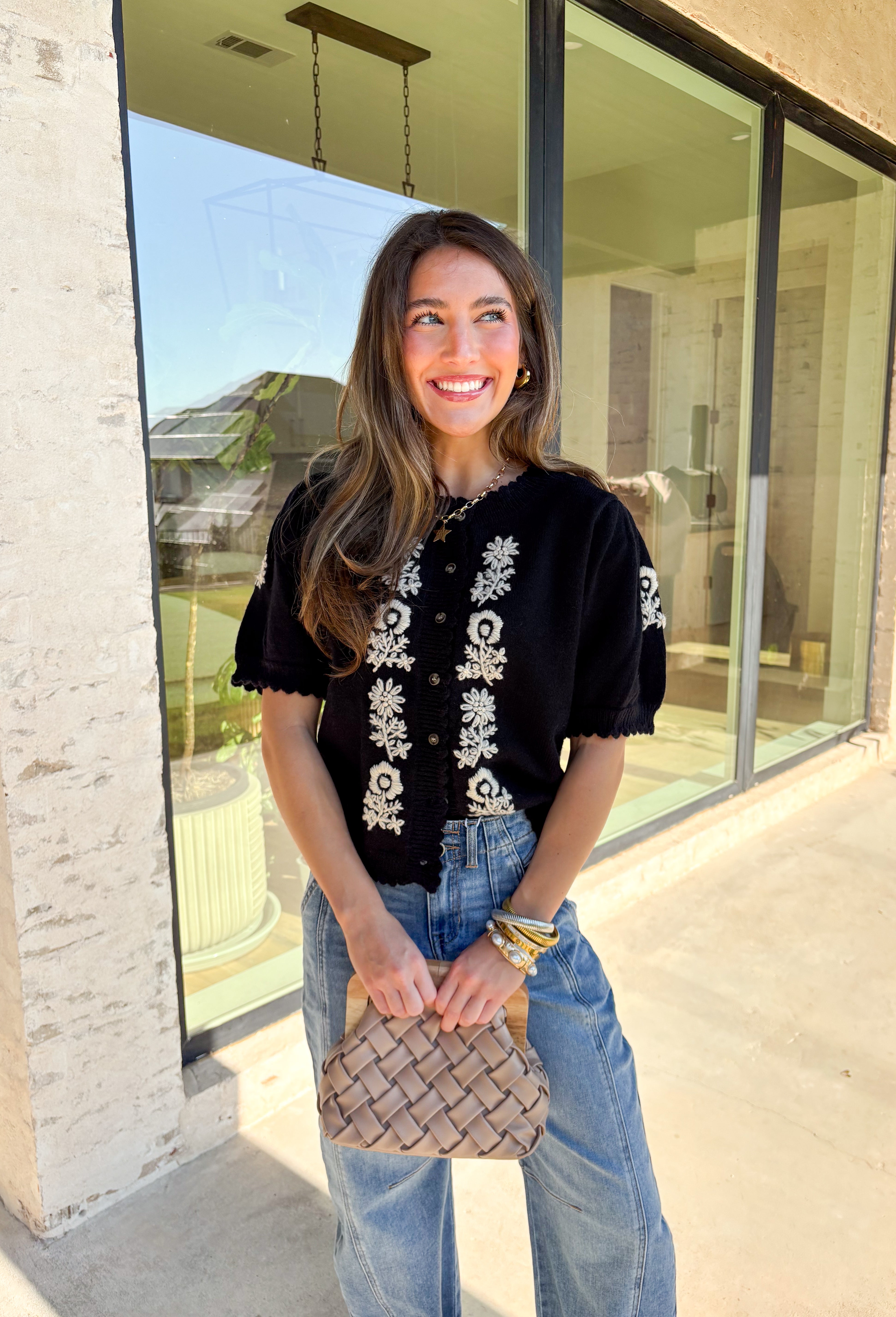 Sweet details and cozy texture make this cardigan a seasonal favorite. Designed in a soft black knit, it’s accented with cream embroidered florals down the front, and on the sleeves for a touch of charm. The scalloped trim along the sleeves, hem, and neckline adds a feminine finish, while the short sleeve and button-down design keep it versatile. An easy layering piece you can style casual or dressed up, this cardigan is the perfect balance of cozy and polished.