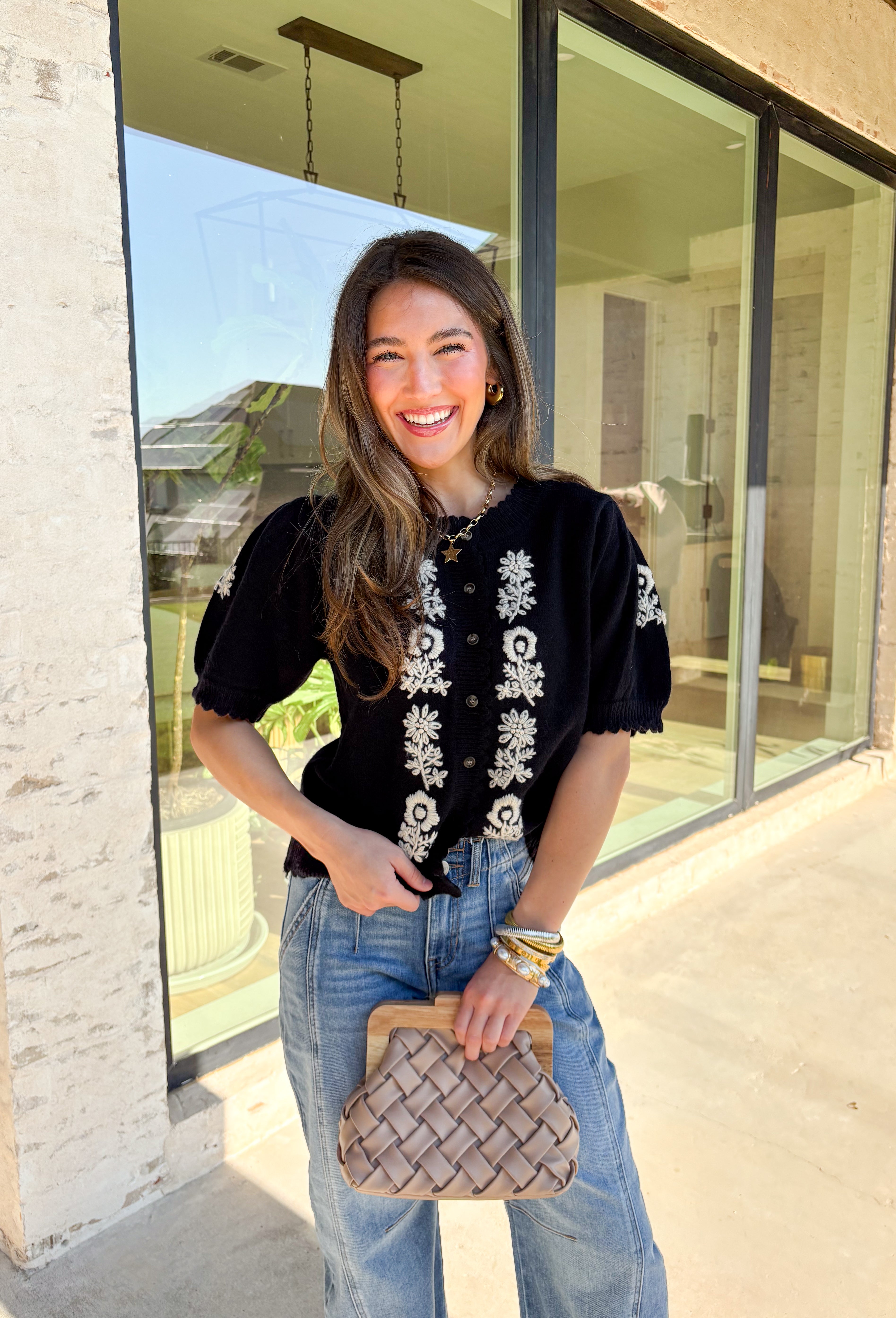 Sweet details and cozy texture make this cardigan a seasonal favorite. Designed in a soft black knit, it’s accented with cream embroidered florals down the front, and on the sleeves for a touch of charm. The scalloped trim along the sleeves, hem, and neckline adds a feminine finish, while the short sleeve and button-down design keep it versatile. An easy layering piece you can style casual or dressed up, this cardigan is the perfect balance of cozy and polished.