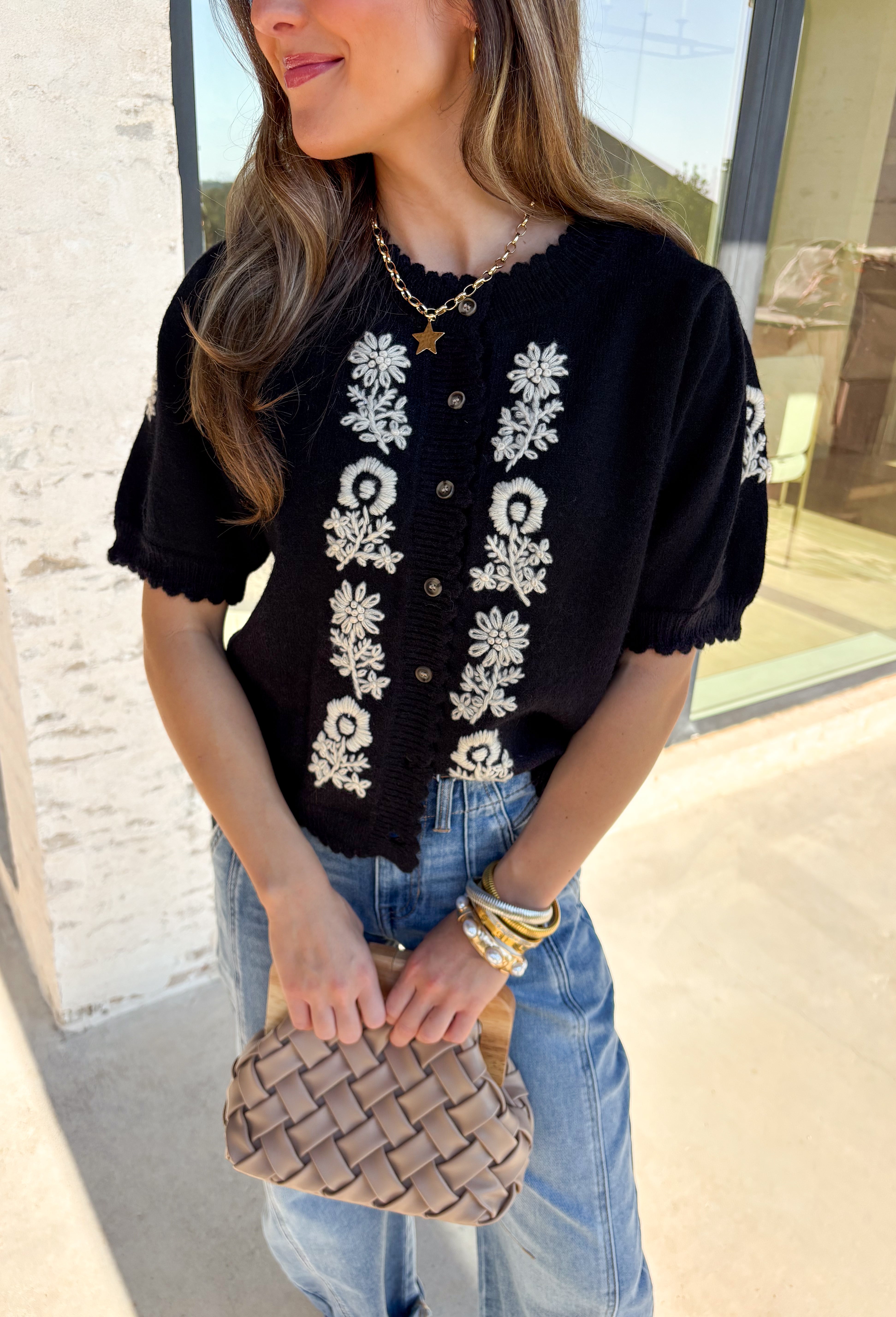 Sweet details and cozy texture make this cardigan a seasonal favorite. Designed in a soft black knit, it’s accented with cream embroidered florals down the front, and on the sleeves for a touch of charm. The scalloped trim along the sleeves, hem, and neckline adds a feminine finish, while the short sleeve and button-down design keep it versatile. An easy layering piece you can style casual or dressed up, this cardigan is the perfect balance of cozy and polished.