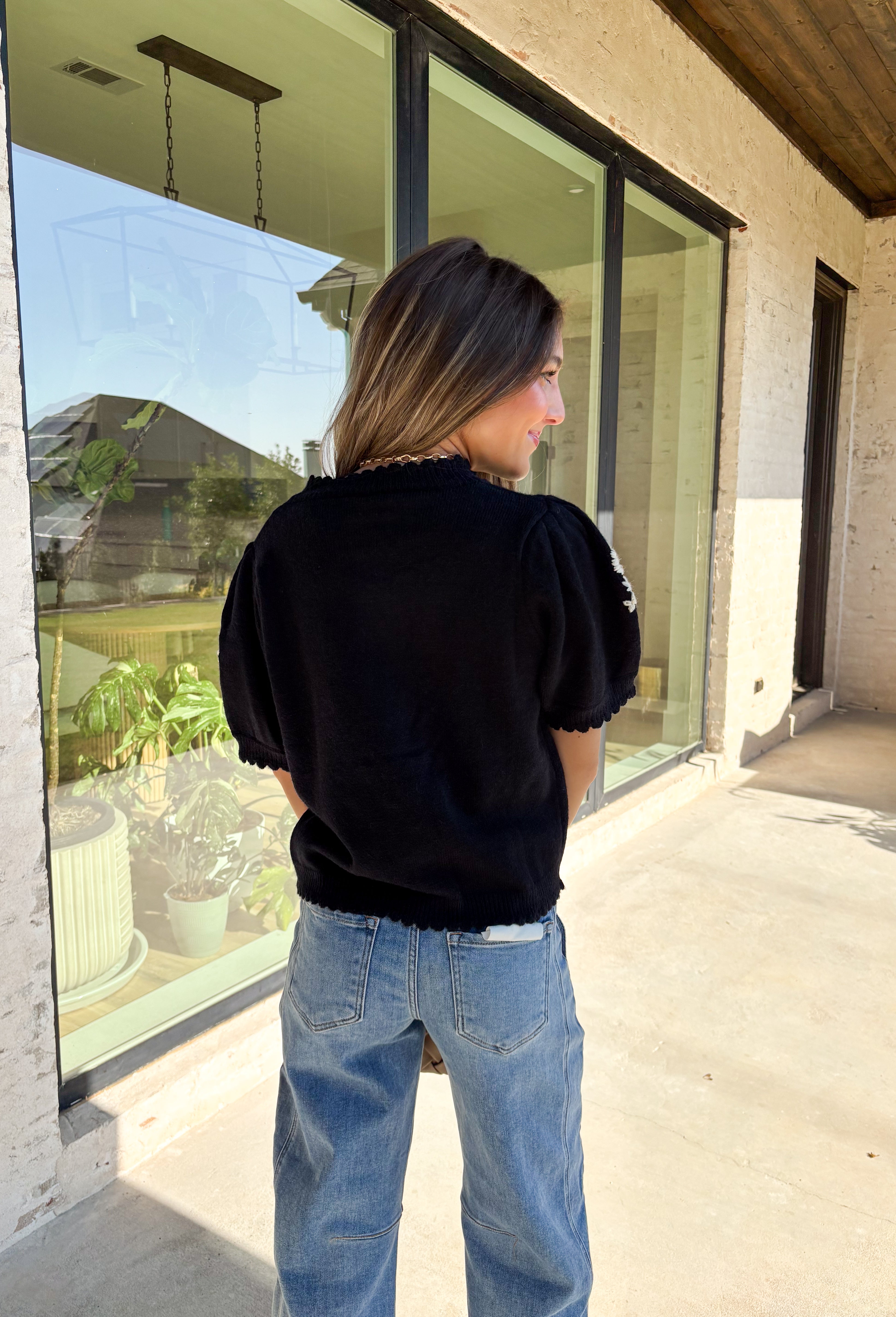 Sweet details and cozy texture make this cardigan a seasonal favorite. Designed in a soft black knit, it’s accented with cream embroidered florals down the front, and on the sleeves for a touch of charm. The scalloped trim along the sleeves, hem, and neckline adds a feminine finish, while the short sleeve and button-down design keep it versatile. An easy layering piece you can style casual or dressed up, this cardigan is the perfect balance of cozy and polished.