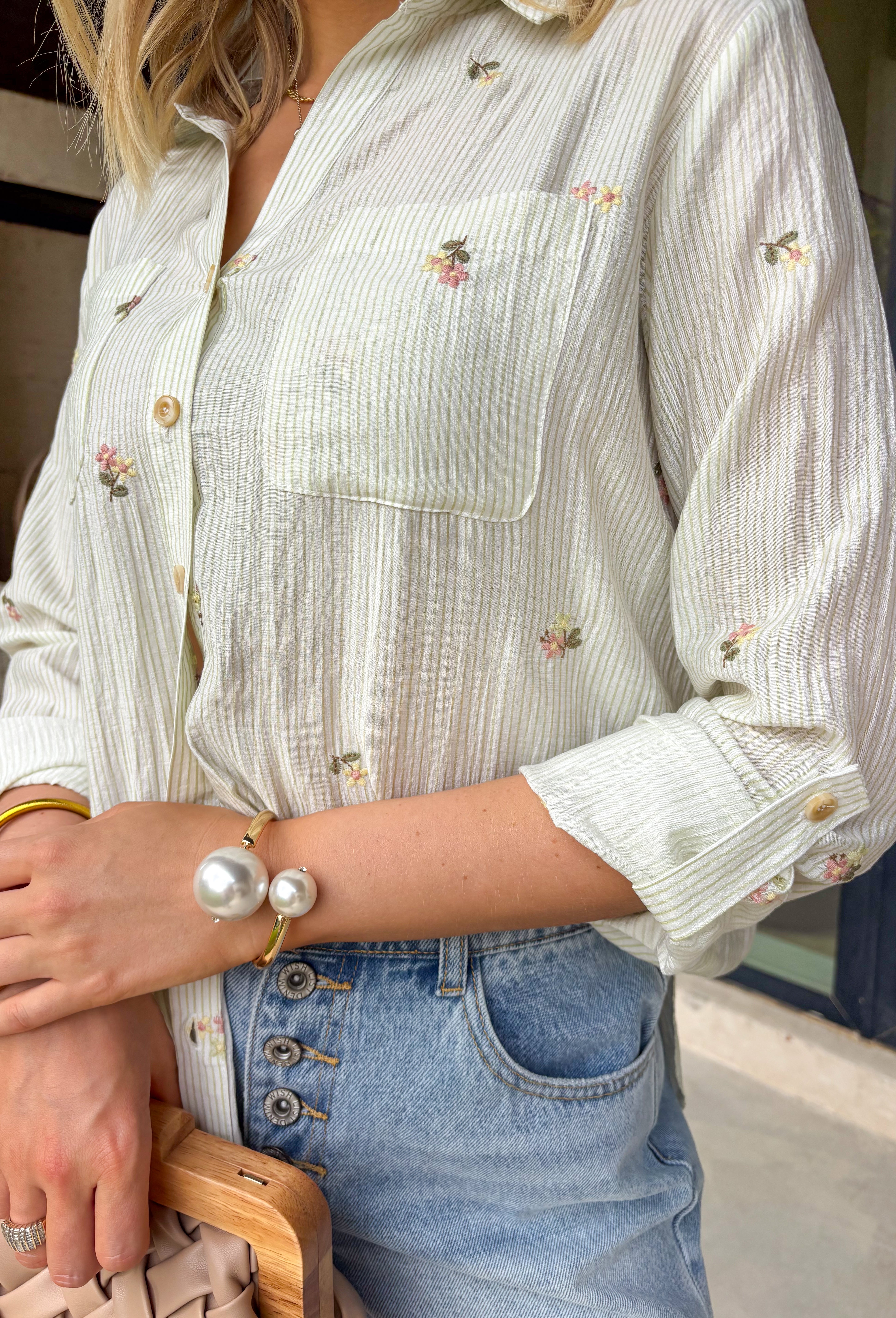 This off white button down is one of those effortlessly pretty pieces that works all summer long! The light olive stripe print paired with delicate floral embroidery gives it a soft, elevated feel while still being easy to style for everyday wear. Designed with a classic collared neckline, front pockets, and cuffed sleeves, it has that timeless button down look with a feminine twist. Lightweight and breathable, it’s perfect for layering over a tank or wearing on its own with denim or shorts. 