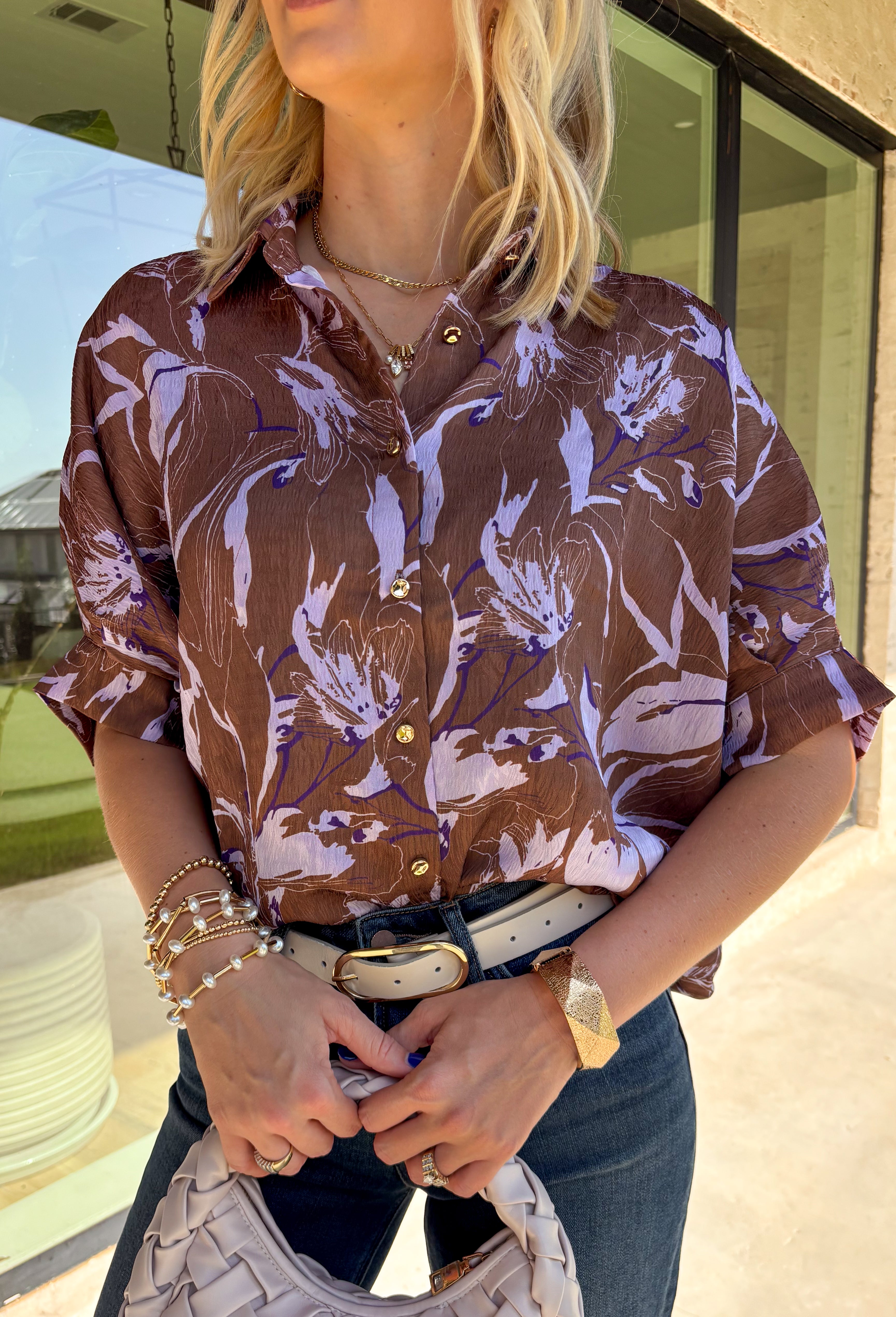 Rich fall shades and standout details make this printed blouse from Entro an easy way to bring a little color into your autumn wardrobe. The warm brown base is accented with lilac and dark purple throughout, creating a unique print that pairs beautifully with the season’s deeper tones. A classic shirt collar and hammered gold buttons dress up the front, while the ¾ dolman sleeves give it a relaxed, comfortable silhouette. 