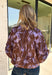 Rich fall shades and standout details make this printed blouse from Entro an easy way to bring a little color into your autumn wardrobe. The warm brown base is accented with lilac and dark purple throughout, creating a unique print that pairs beautifully with the season’s deeper tones. A classic shirt collar and hammered gold buttons dress up the front, while the ¾ dolman sleeves give it a relaxed, comfortable silhouette. 