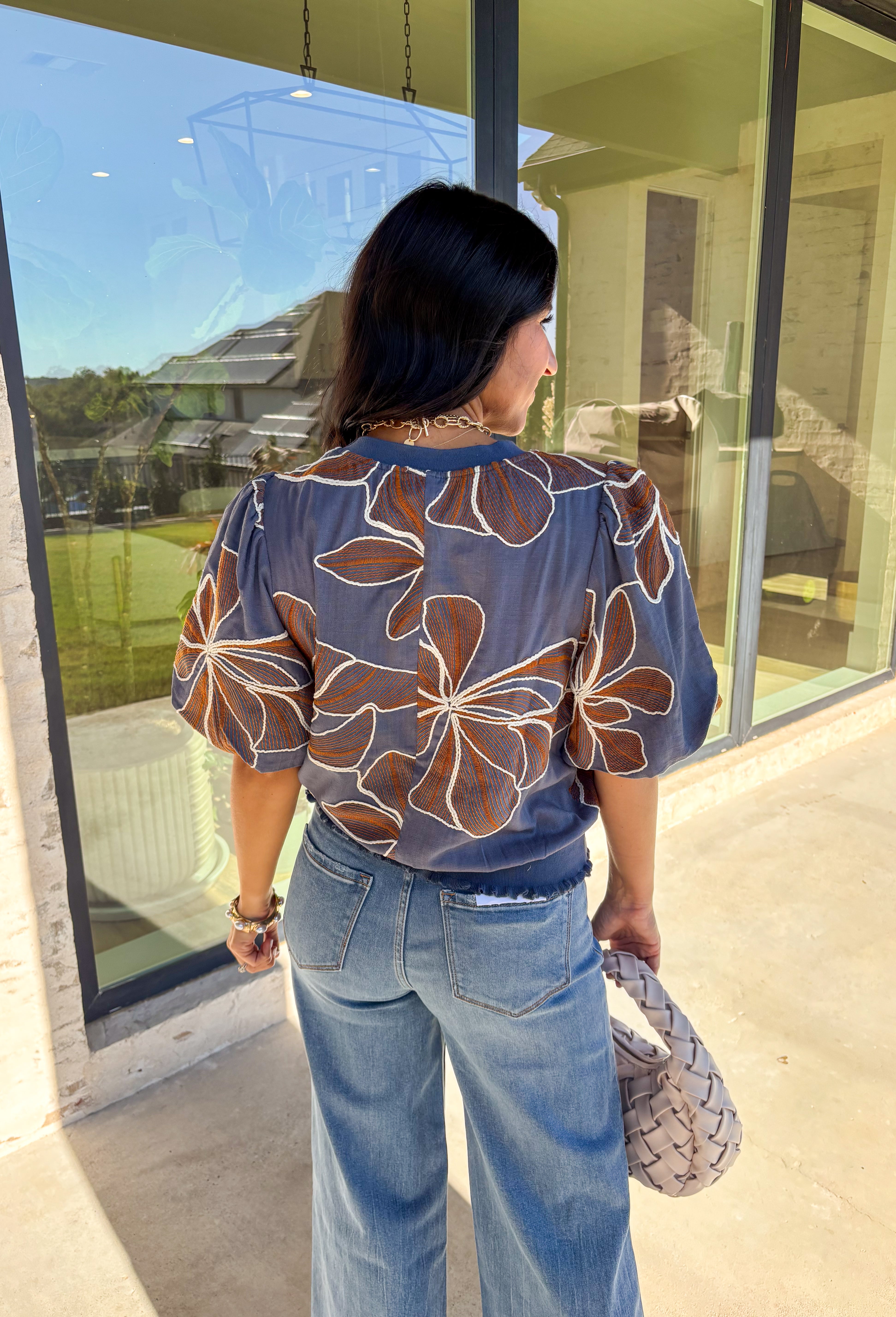 Effortlessly charming, this blue puff sleeve top by Voy is a fall favorite with a touch of whimsy. Designed with an oversized rust and white embroidered floral pattern throughout, it brings texture and color to your everyday look. The short puff sleeves and lettuce hem add a feminine finish, while the soft linen-blend fabric keeps it lightweight and breathable. Perfect for pairing with denim or skirts all season long.