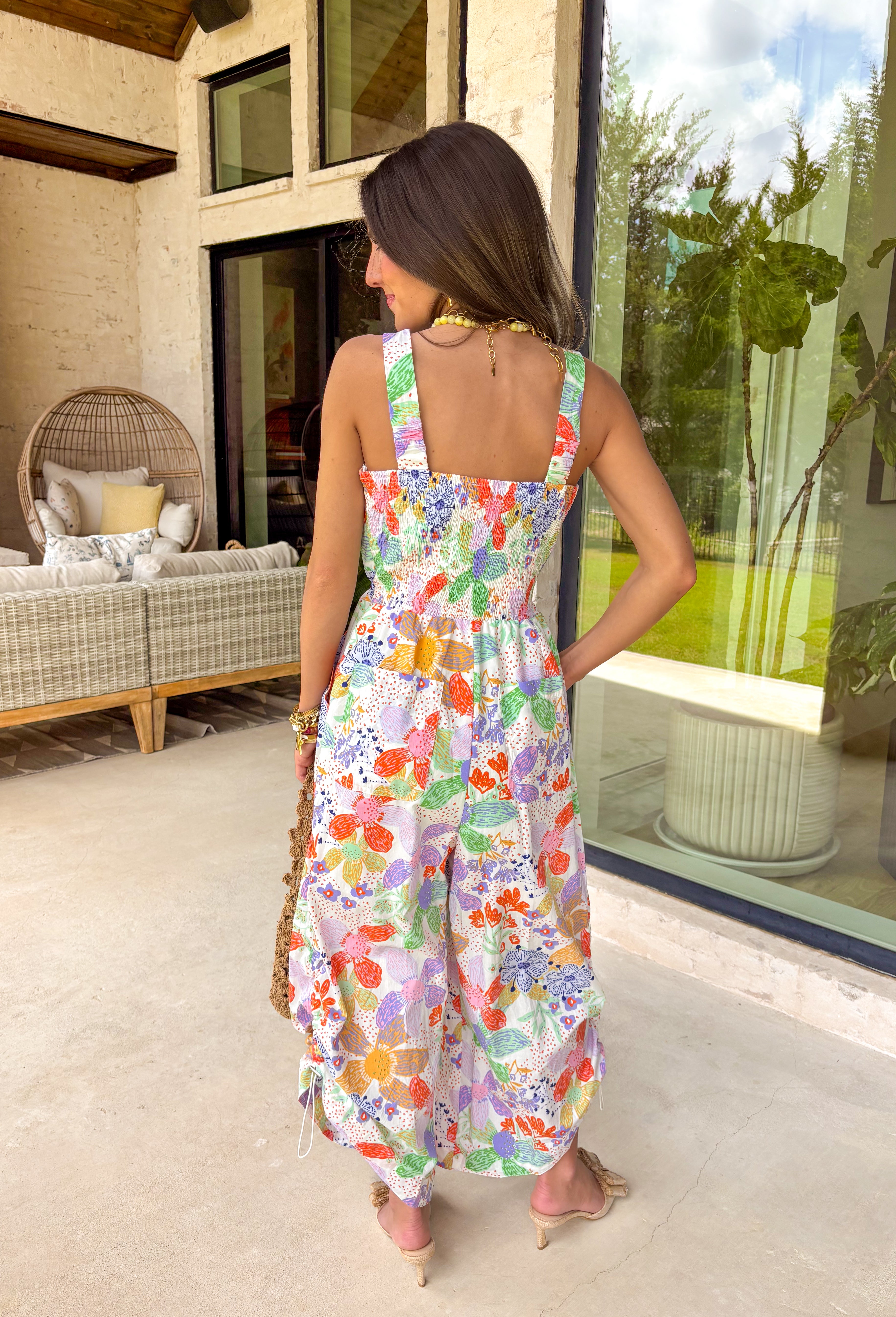 Say hello to your new one-and-done spring outfit! This white jumpsuit is covered in the prettiest colorful floral print with pops of green, orange, purple, pink, and yellow—basically sunshine in clothing form. The square neckline gives it a clean, flattering shape, while the smocked back keeps it comfy and flexible. Finished with side pockets (yes please), a side zipper for easy on-and-off, and adjustable ties at the waist and ankles, this piece is made for everything from weekend plans to vacation days.