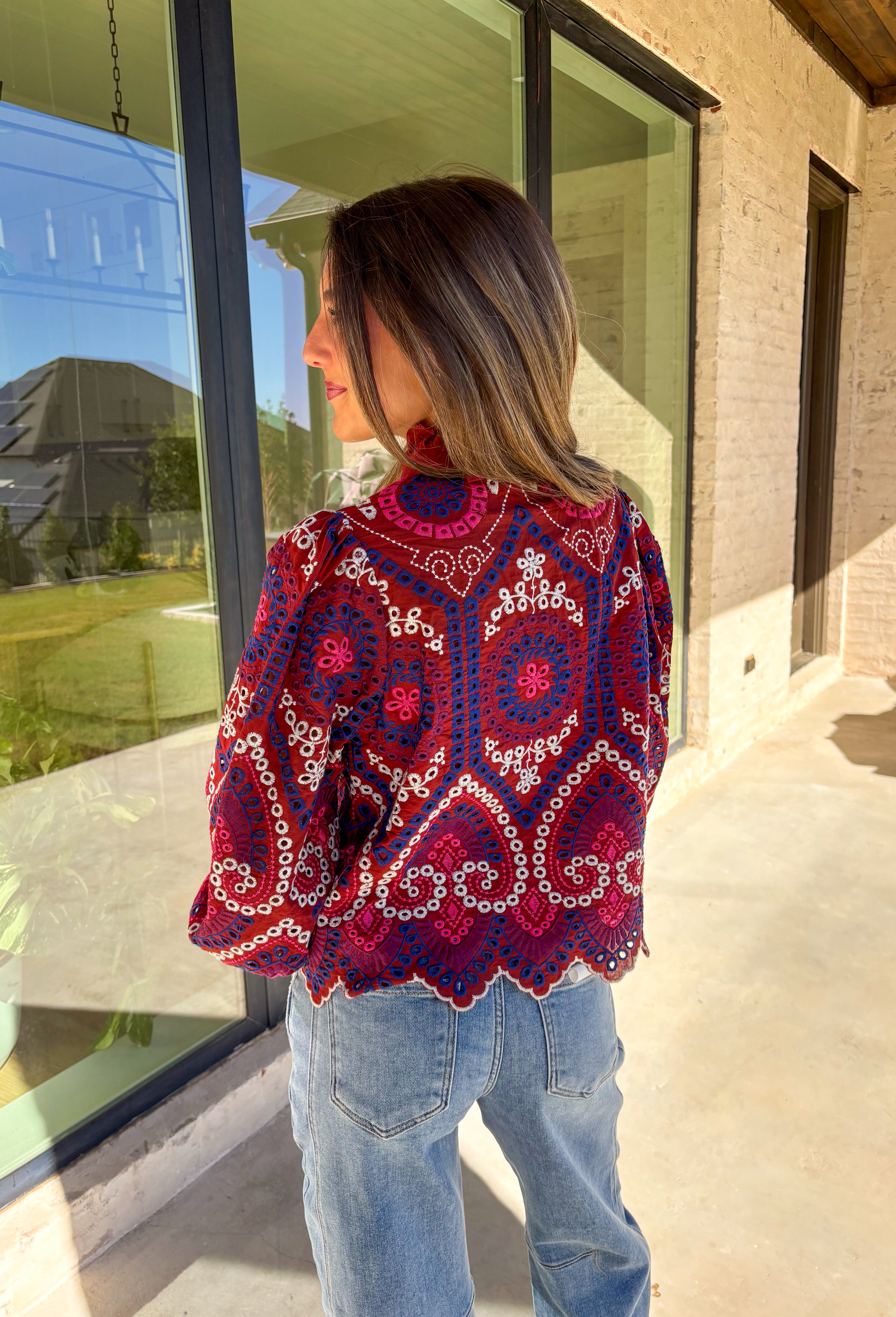Bring color and texture to your fall wardrobe with this brick long sleeve top by Entro. The vibrant embroidered print in royal blue, white, pink, and purple adds a playful pop against the warm brick base. A ruffled neckline and trim along the front pair beautifully with the half button-down design, while the scalloped hem gives it a soft, feminine finish. Lightweight and full of detail, this top is perfect for adding a touch of boho charm to your seasonal looks.