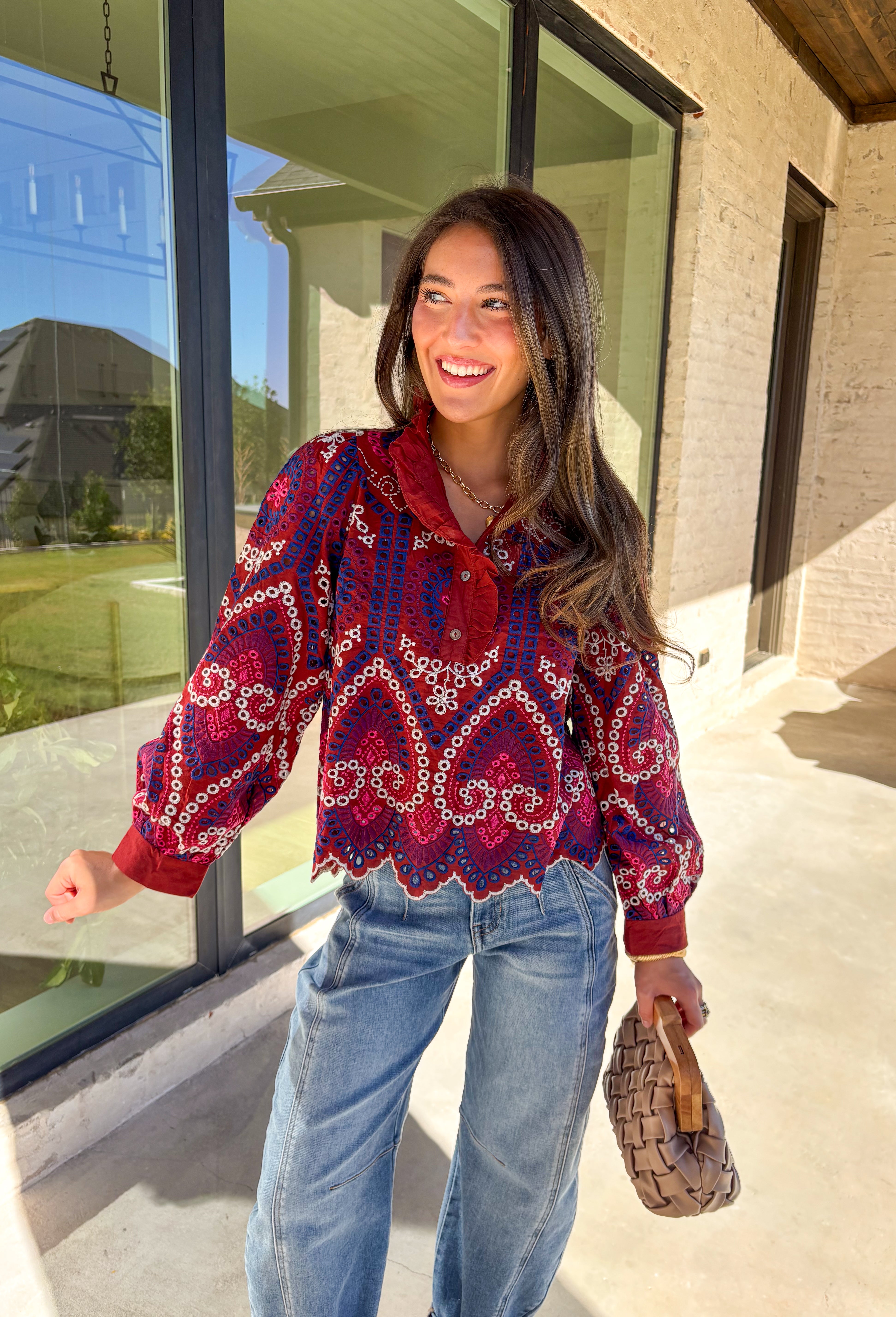 Bring color and texture to your fall wardrobe with this brick long sleeve top by Entro. The vibrant embroidered print in royal blue, white, pink, and purple adds a playful pop against the warm brick base. A ruffled neckline and trim along the front pair beautifully with the half button-down design, while the scalloped hem gives it a soft, feminine finish. Lightweight and full of detail, this top is perfect for adding a touch of boho charm to your seasonal looks.
