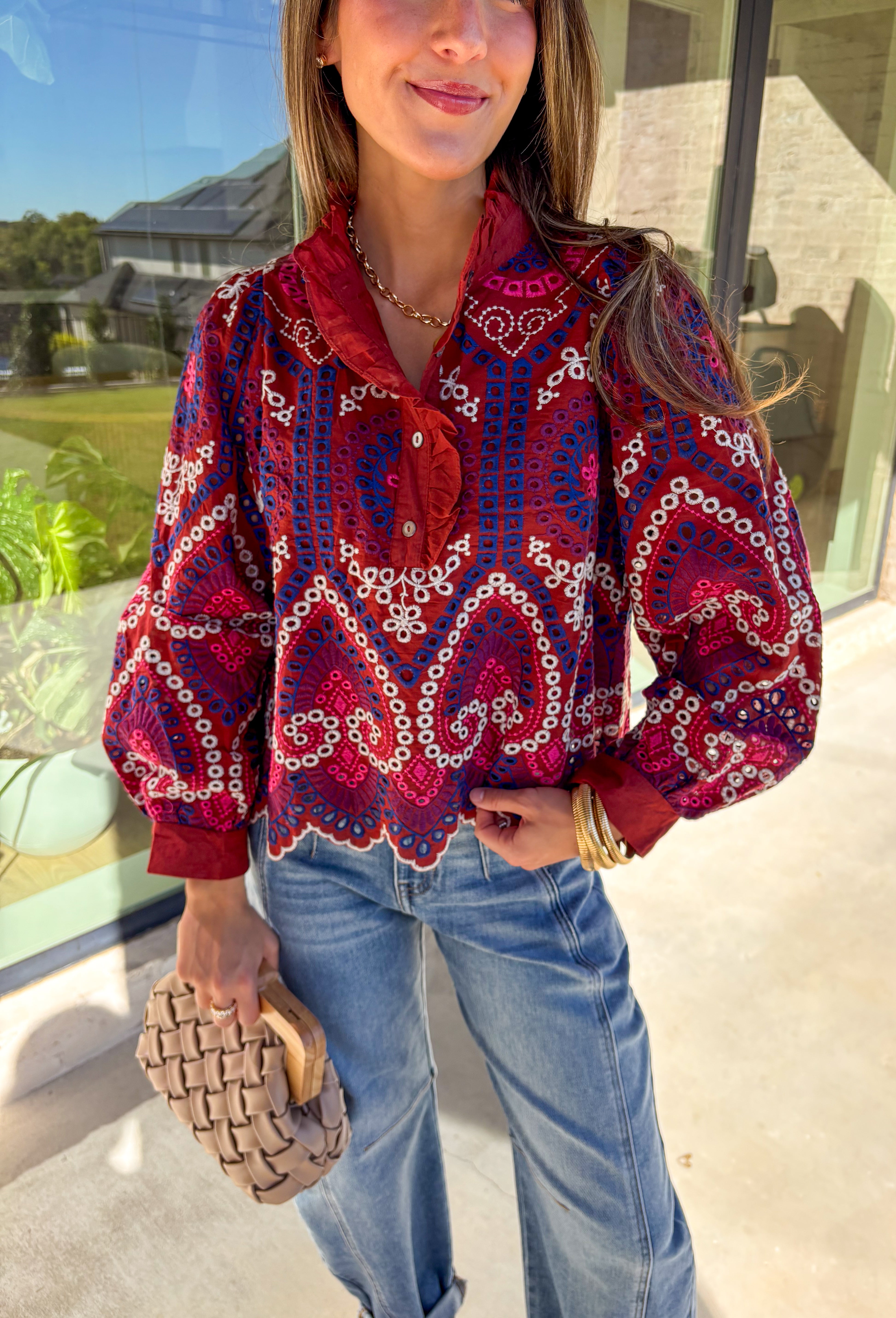 Bring color and texture to your fall wardrobe with this brick long sleeve top by Entro. The vibrant embroidered print in royal blue, white, pink, and purple adds a playful pop against the warm brick base. A ruffled neckline and trim along the front pair beautifully with the half button-down design, while the scalloped hem gives it a soft, feminine finish. Lightweight and full of detail, this top is perfect for adding a touch of boho charm to your seasonal looks.