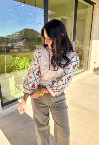 This ecru long sleeve top by Entro brings an elegant touch to your fall wardrobe with its beautifully embroidered floral sleeves. Detailed in shades of burgundy, rust, blue, and green, the embroidery stands out perfectly against the soft neutral base. The contrast scallop trim neckline adds a sweet finishing touch, giving this pullover top a timeless and feminine feel. Lightweight and easy to style, it’s a lovely go-to piece for both casual days and dressed-up outings.