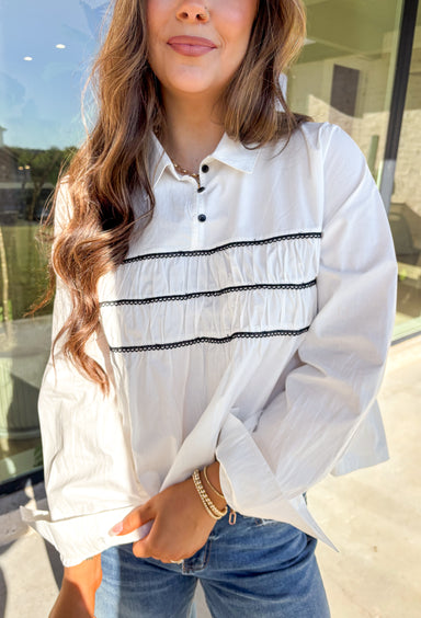 A polished essential with a playful twist—this white long sleeve top is designed with bold black scalloped trim running across the front and around the back for eye-catching contrast. The collared neckline and button detail give it a timeless look, while the crisp cotton fabric keeps it breathable and easy to wear. Perfect for layering or styling solo, this top transitions effortlessly from office days to cozy outings.