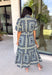 Bring effortless elegance to your wardrobe with this beautifully detailed dress from Entro. Designed with a soft light blue backdrop and an eye-catching abstract print in shades of navy, white, and cream, this timeless piece is perfect for everything from brunch dates to special gatherings. A subtle ruffle neckline adds a feminine touch, while the black buttons outlined in gold create an elevated, polished finish.