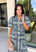 Bring effortless elegance to your wardrobe with this beautifully detailed dress from Entro. Designed with a soft light blue backdrop and an eye-catching abstract print in shades of navy, white, and cream, this timeless piece is perfect for everything from brunch dates to special gatherings. A subtle ruffle neckline adds a feminine touch, while the black buttons outlined in gold create an elevated, polished finish. 