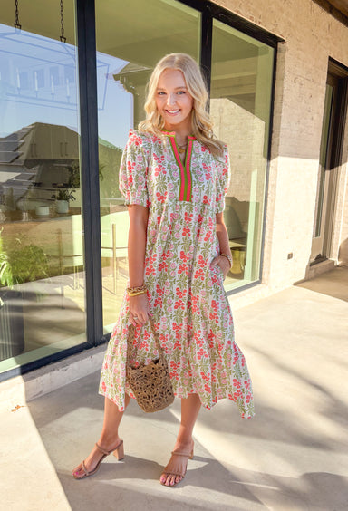 Soft, cheerful, and made for spring days, this off-white midi dress by Entro is full of sweet, standout details. Featuring a floral print in shades of green, coral, and pink, it brings the perfect pop of color while still feeling light and easy to wear. Green and coral trim along the front adds a fun contrast touch, while smocked sleeves and a ruffle shoulder detail give it that extra feminine finish. Fully lined with side pockets, this dress is equal parts pretty and practical—perfect for brunch, showers, 