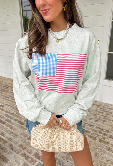 This heather grey pullover is the perfect cozy-meets-festive piece for your summer celebrations! Featuring red and white stripes with a blue and white gingham flag, it brings a fun, playful take on classic patriotic style. The mock neck adds a slightly elevated feel, while the soft cotton fabric keeps it comfortable for those breezy summer nights—think fireworks, lake evenings, or early morning coffee runs. It’s an easy throw-on piece that still feels festive and put together. 