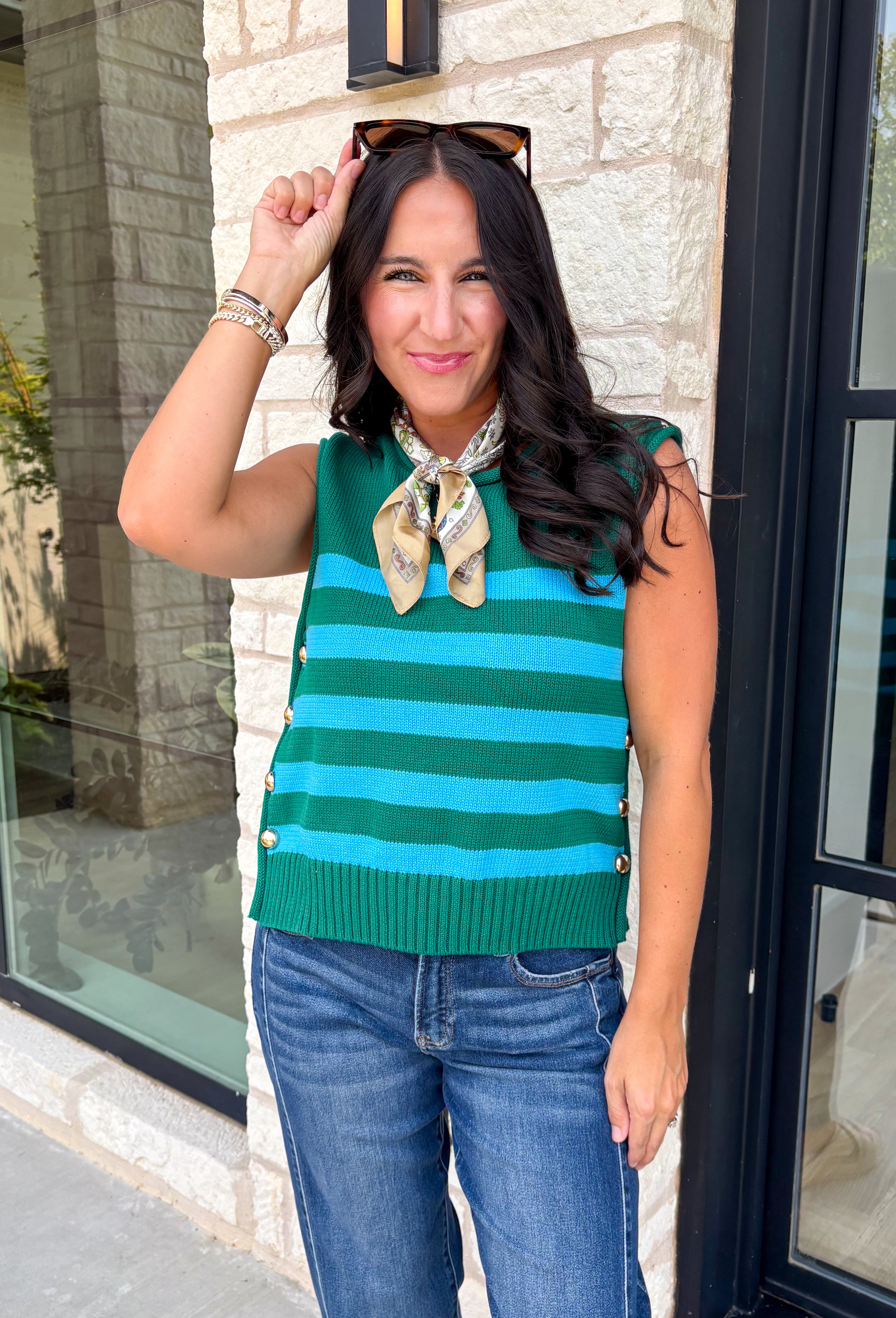 Classic stripes get a bold fall refresh with this cozy sleeveless sweater! Featuring a rich pine green knit with vibrant blue stripes, this sleeveless top is an easy way to add color to your seasonal wardrobe. Functional gold button closures along the sides add a unique, elevated touch, while the ribbed crew neckline and hem give it a timeless finish.