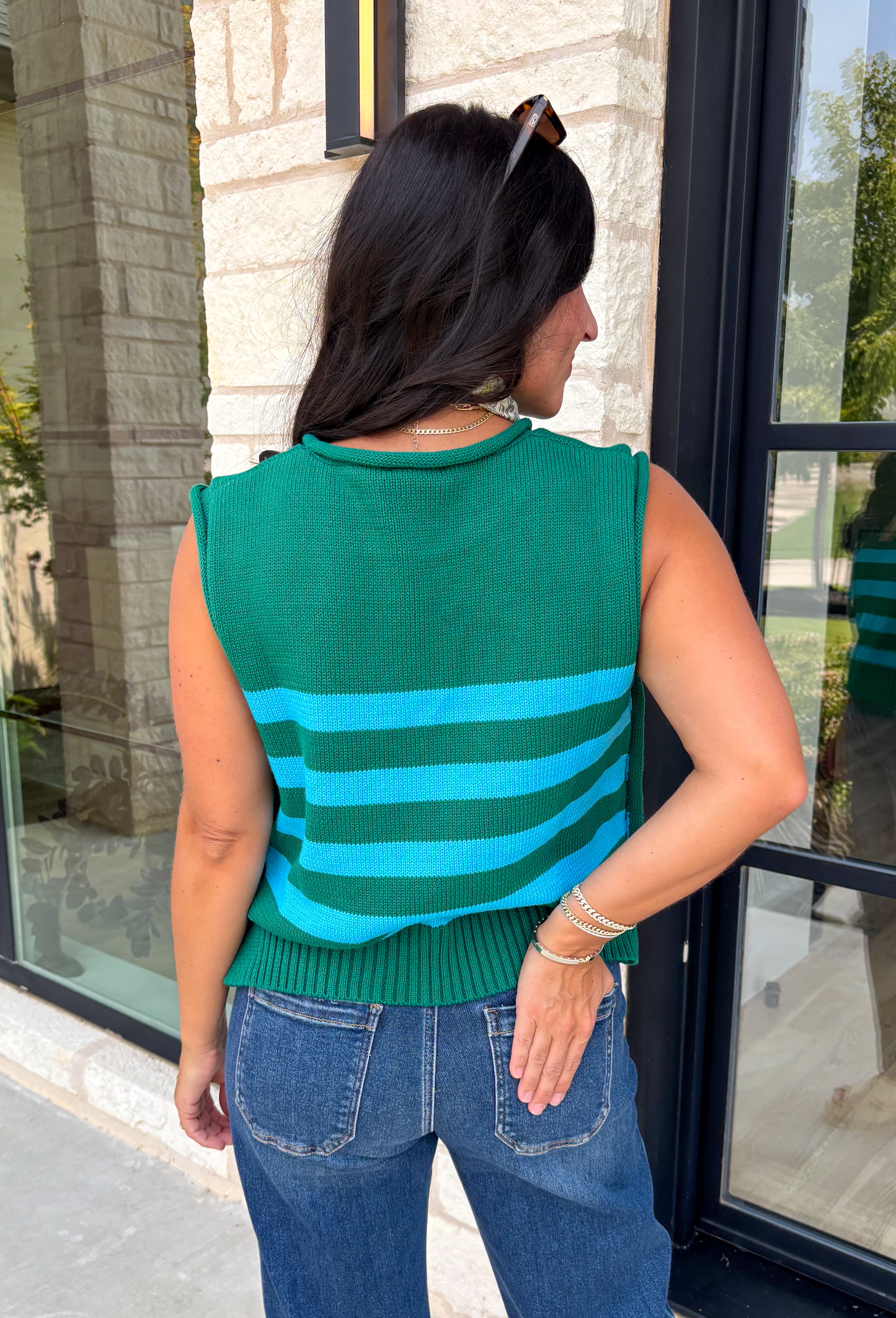 Classic stripes get a bold fall refresh with this cozy sleeveless sweater! Featuring a rich pine green knit with vibrant blue stripes, this sleeveless top is an easy way to add color to your seasonal wardrobe. Functional gold button closures along the sides add a unique, elevated touch, while the ribbed crew neckline and hem give it a timeless finish.