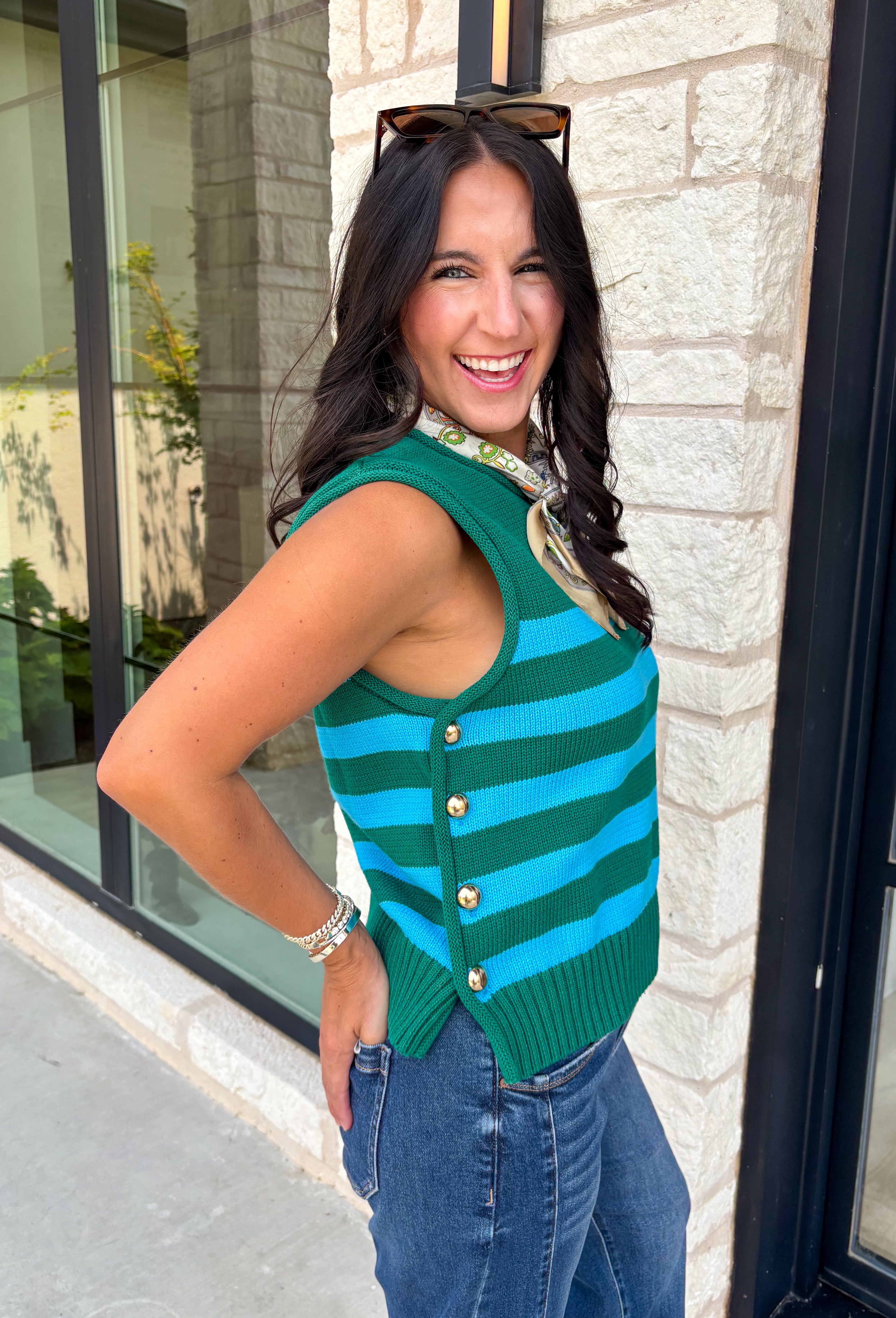 Classic stripes get a bold fall refresh with this cozy sleeveless sweater! Featuring a rich pine green knit with vibrant blue stripes, this sleeveless top is an easy way to add color to your seasonal wardrobe. Functional gold button closures along the sides add a unique, elevated touch, while the ribbed crew neckline and hem give it a timeless finish.