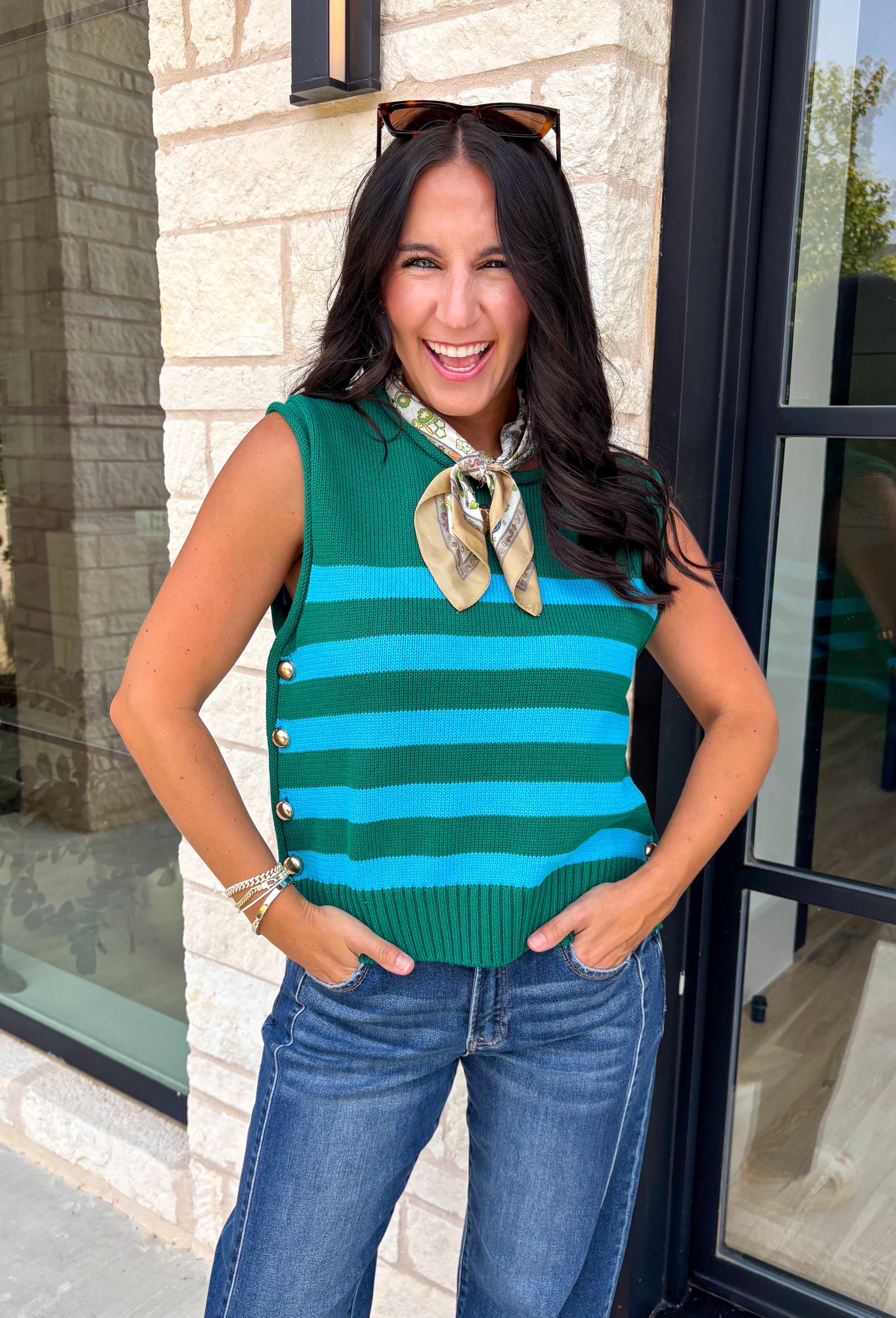 Classic stripes get a bold fall refresh with this cozy sleeveless sweater! Featuring a rich pine green knit with vibrant blue stripes, this sleeveless top is an easy way to add color to your seasonal wardrobe. Functional gold button closures along the sides add a unique, elevated touch, while the ribbed crew neckline and hem give it a timeless finish.