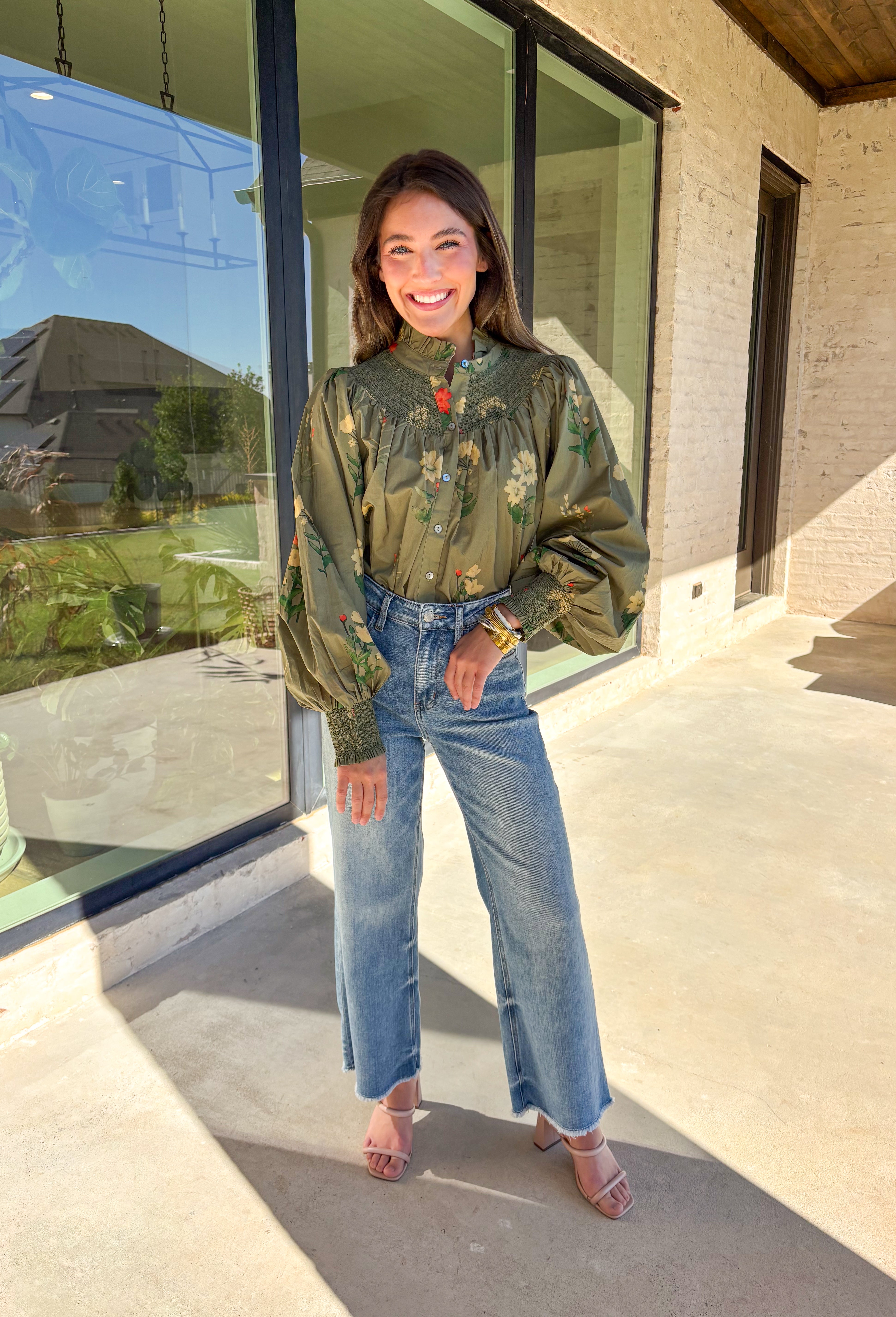 Romantic and timeless, this olive floral top by Entro is full of fall charm. The smocked yoke and ruffled mock neckline add a soft, feminine touch, while the button-front detail brings in classic appeal. Smocked cuffs create a subtle billowed sleeve effect, giving this piece a flattering silhouette. With shades of autumn florals throughout, it’s an easy choice for both casual days and dressier occasions.