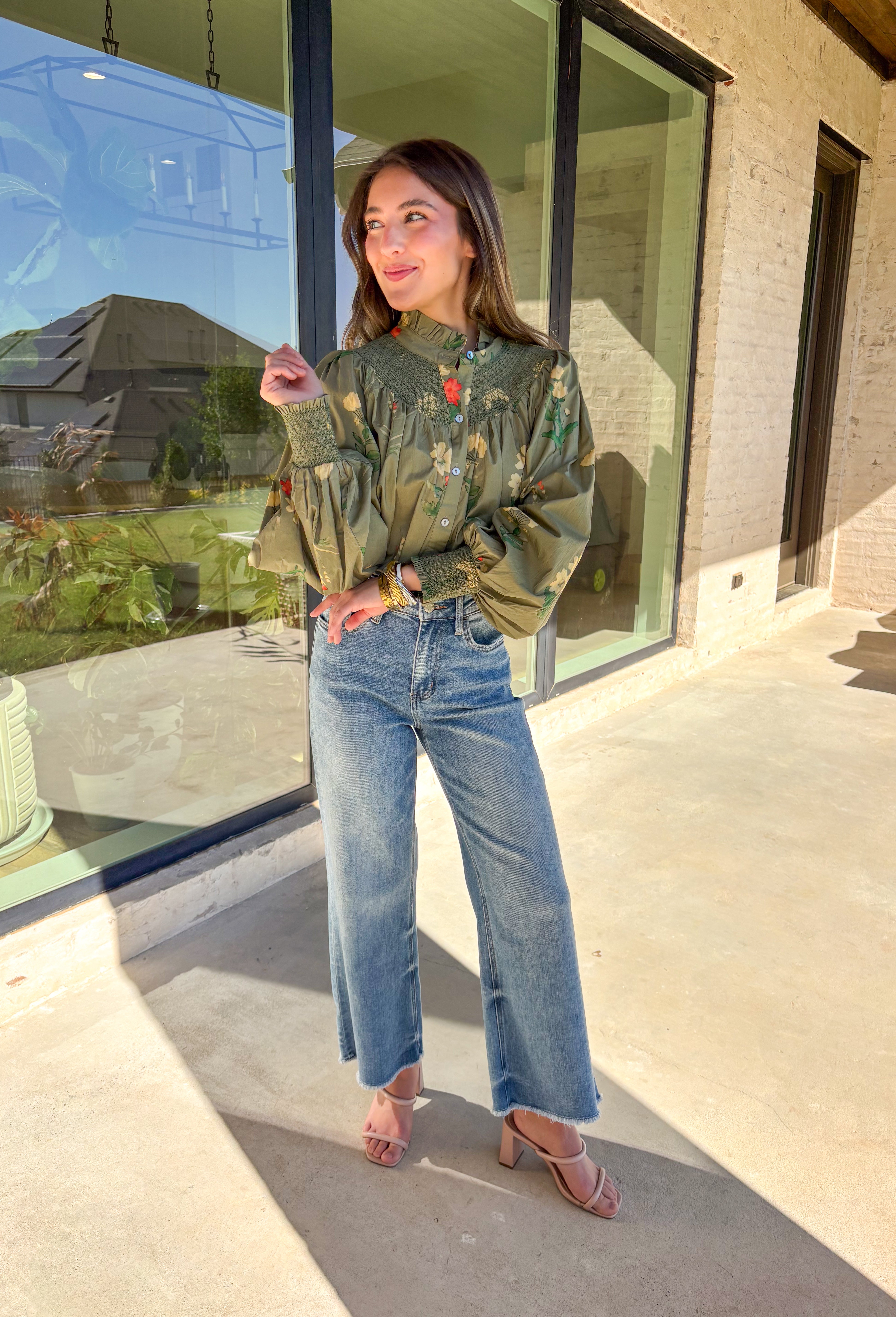 Romantic and timeless, this olive floral top by Entro is full of fall charm. The smocked yoke and ruffled mock neckline add a soft, feminine touch, while the button-front detail brings in classic appeal. Smocked cuffs create a subtle billowed sleeve effect, giving this piece a flattering silhouette. With shades of autumn florals throughout, it’s an easy choice for both casual days and dressier occasions.