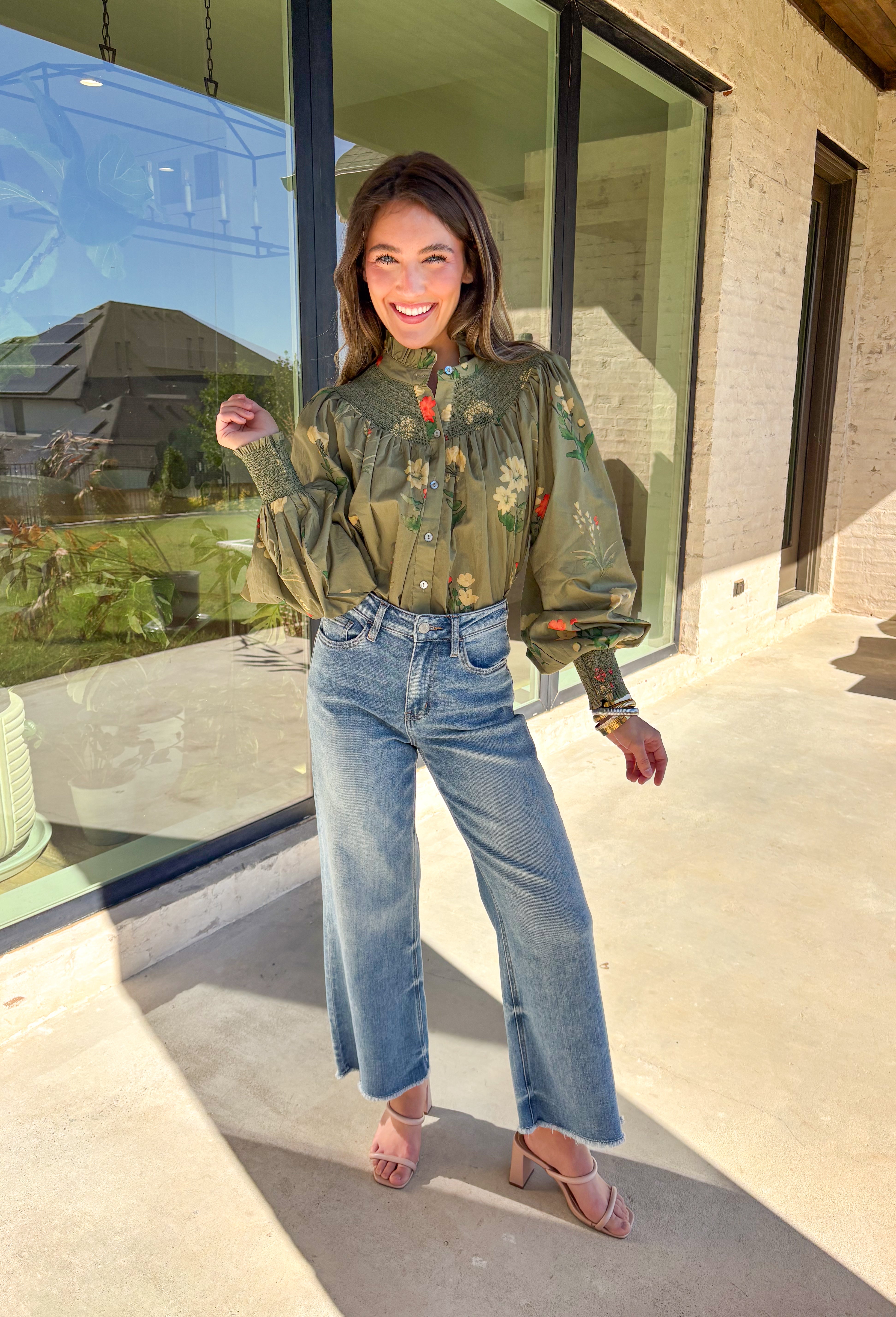 Romantic and timeless, this olive floral top by Entro is full of fall charm. The smocked yoke and ruffled mock neckline add a soft, feminine touch, while the button-front detail brings in classic appeal. Smocked cuffs create a subtle billowed sleeve effect, giving this piece a flattering silhouette. With shades of autumn florals throughout, it’s an easy choice for both casual days and dressier occasions.