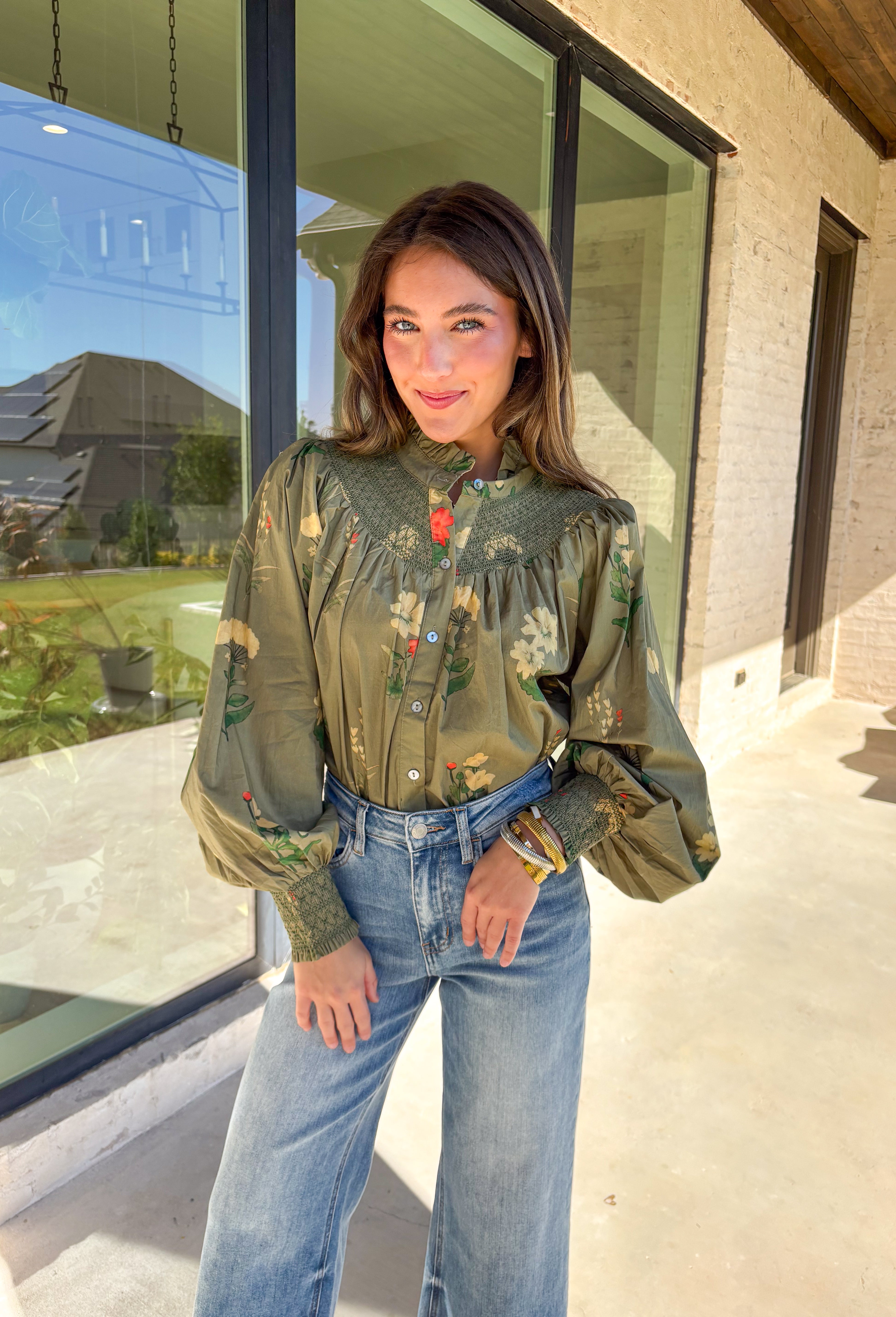 Romantic and timeless, this olive floral top by Entro is full of fall charm. The smocked yoke and ruffled mock neckline add a soft, feminine touch, while the button-front detail brings in classic appeal. Smocked cuffs create a subtle billowed sleeve effect, giving this piece a flattering silhouette. With shades of autumn florals throughout, it’s an easy choice for both casual days and dressier occasions.