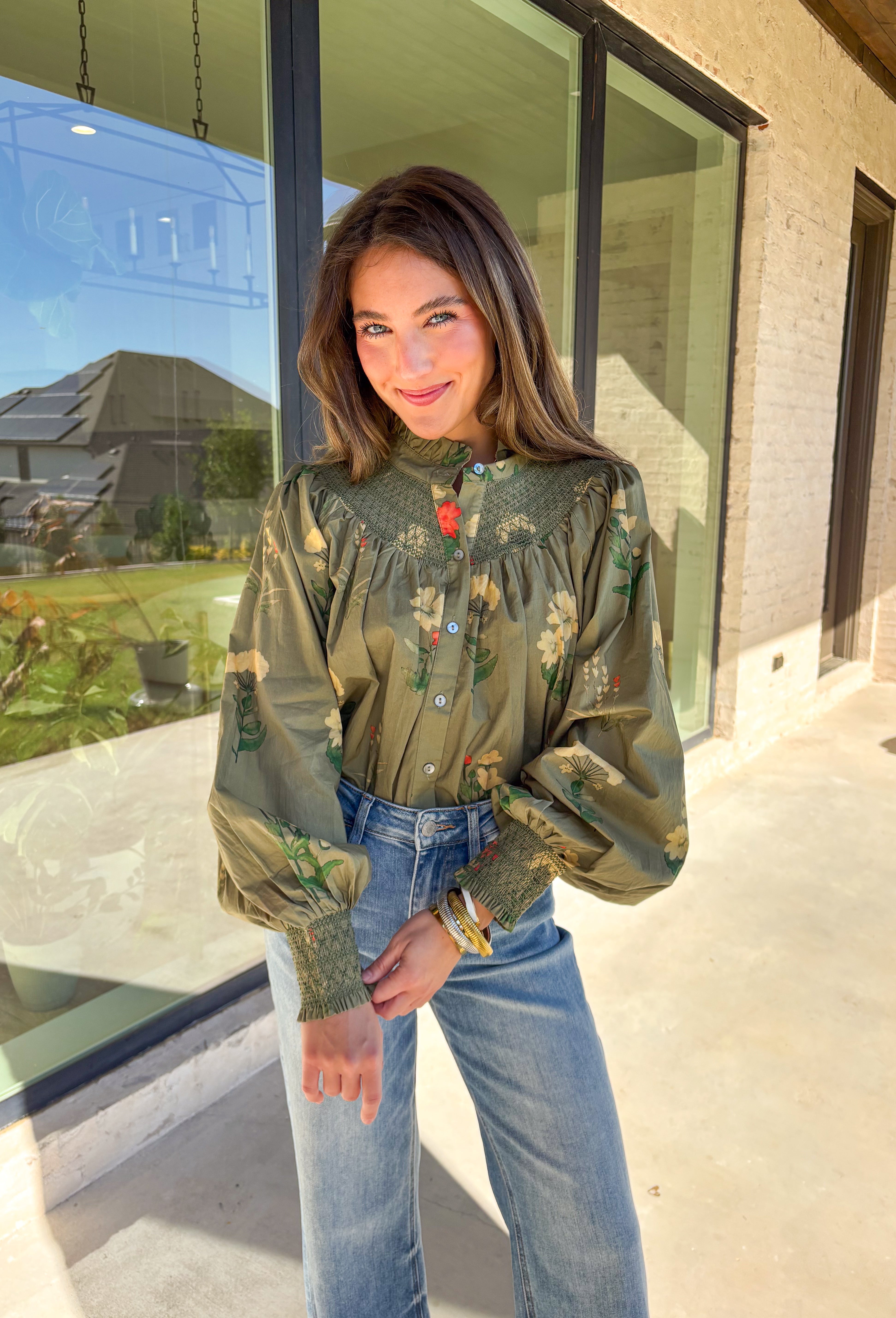 Romantic and timeless, this olive floral top by Entro is full of fall charm. The smocked yoke and ruffled mock neckline add a soft, feminine touch, while the button-front detail brings in classic appeal. Smocked cuffs create a subtle billowed sleeve effect, giving this piece a flattering silhouette. With shades of autumn florals throughout, it’s an easy choice for both casual days and dressier occasions.