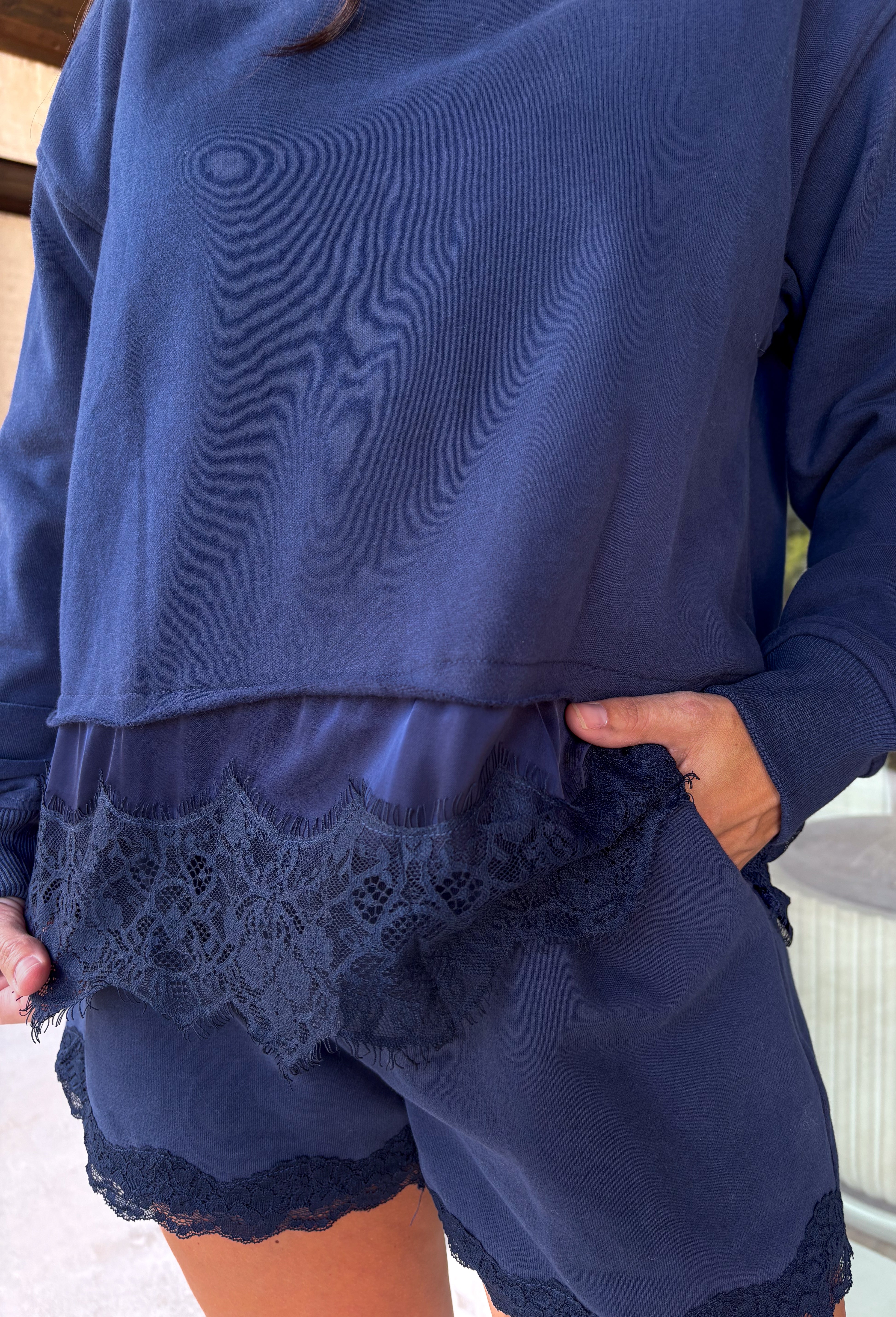 Cozy gets a pretty little upgrade with this navy sweatshirt from Sunday Edition. The classic long sleeve silhouette is finished with a lace hem, adding a feminine touch to an otherwise casual favorite. A soft fleece lining keeps it extra comfortable as chilly fall days start turning into winter weather. Pair it with the matching shorts for a cute coordinated set that’s perfect for relaxing, traveling, or casual weekend plans, or mix it into your closet with denim for an easy everyday outfit. 