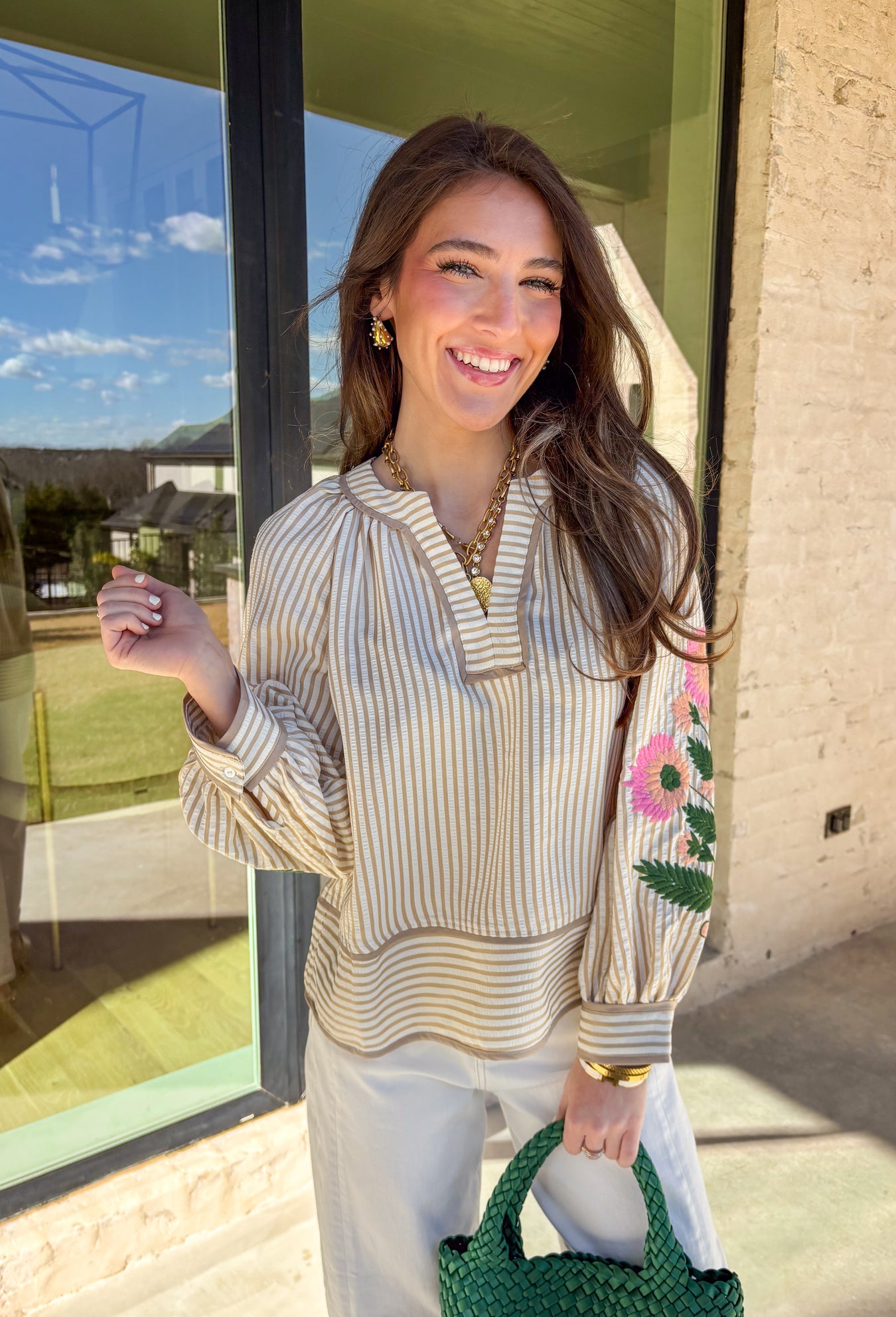 Classic stripes with a spring twist—this tan and off-white striped top by Entro is full of charm and elevated detail. Featuring a band collar v-neck with contrast binding, it has a polished look that’s still easy and effortless. The 3/4 puff sleeves steal the show with colorful floral embroidery in shades of pink, peach, and green, adding the prettiest pop of color and texture. Finished with button cuffs, this top is perfect for dressing up denim or adding a little something special to your everyday spring 