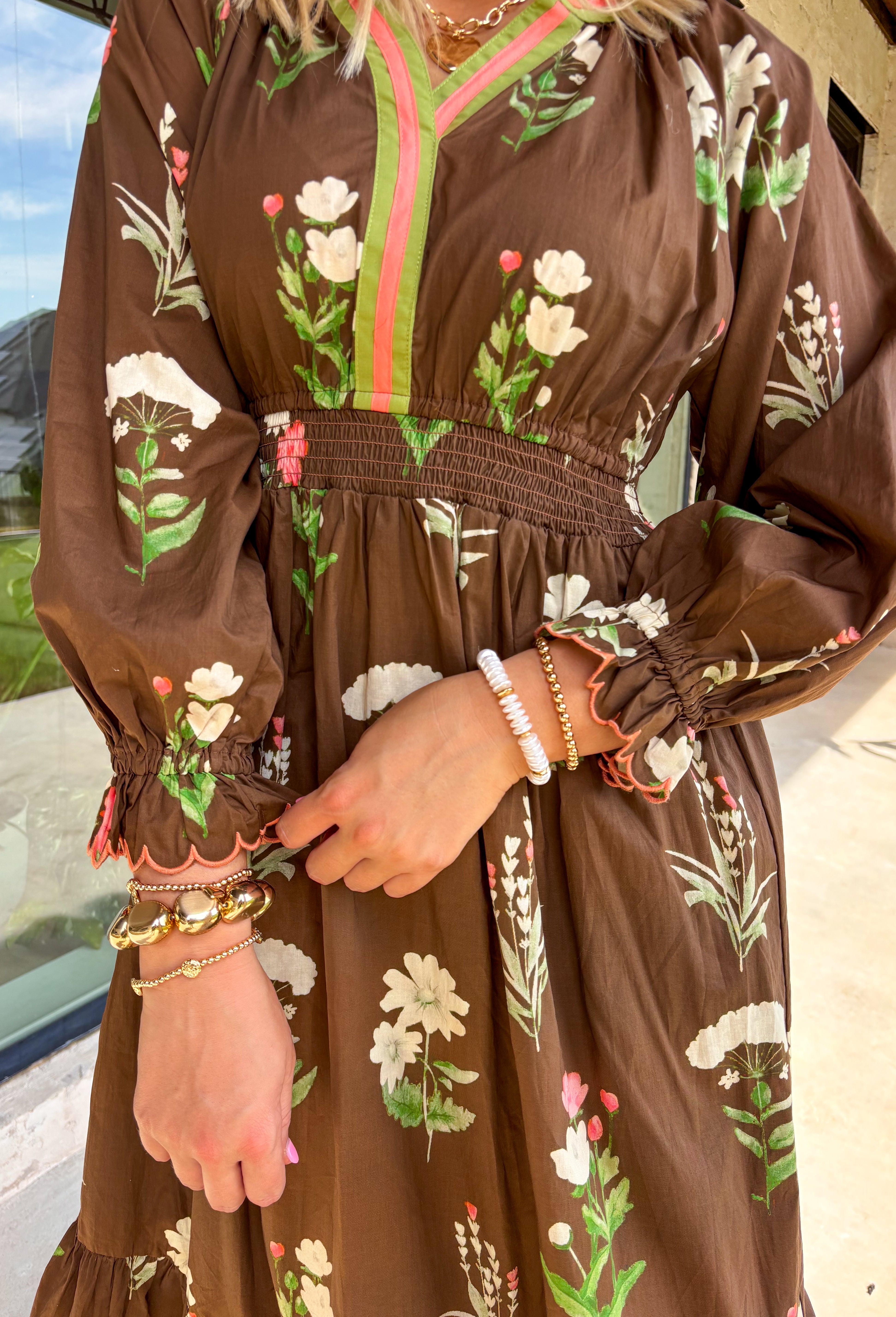This brown floral midi dress is everything we love about fall—rich tones, effortless comfort, and just the right amount of charm. Designed with a flattering elastic waist and scalloped sleeve detail, this long sleeve beauty features a neutral floral print with pops of olive, cream, and coral. The olive and coral trim along the neckline and along the front add a pop of contrast that pulls it all together. It's the kind of dress you'll reach for on repeat this season!