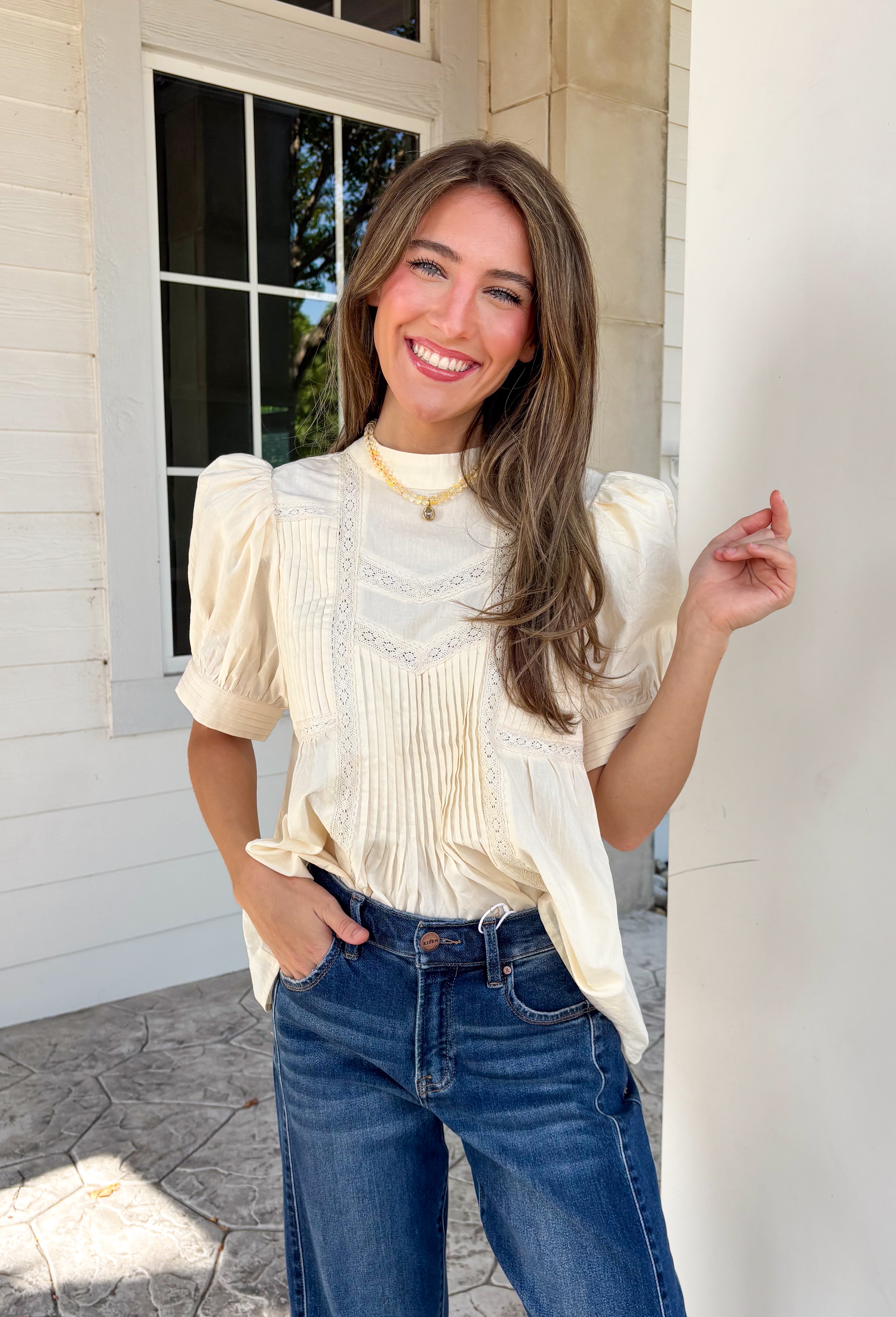 Soft, feminine, and effortlessly timeless, this beautiful ecru top is the kind of piece you'll treasure season after season! Crafted from breathable cotton, it features delicate lace detailing and chic pleating throughout for a look that's both romantic and refined. The puff sleeves add just the right amount of charm, while the keyhole button closure at the back provides a graceful finishing touch. 