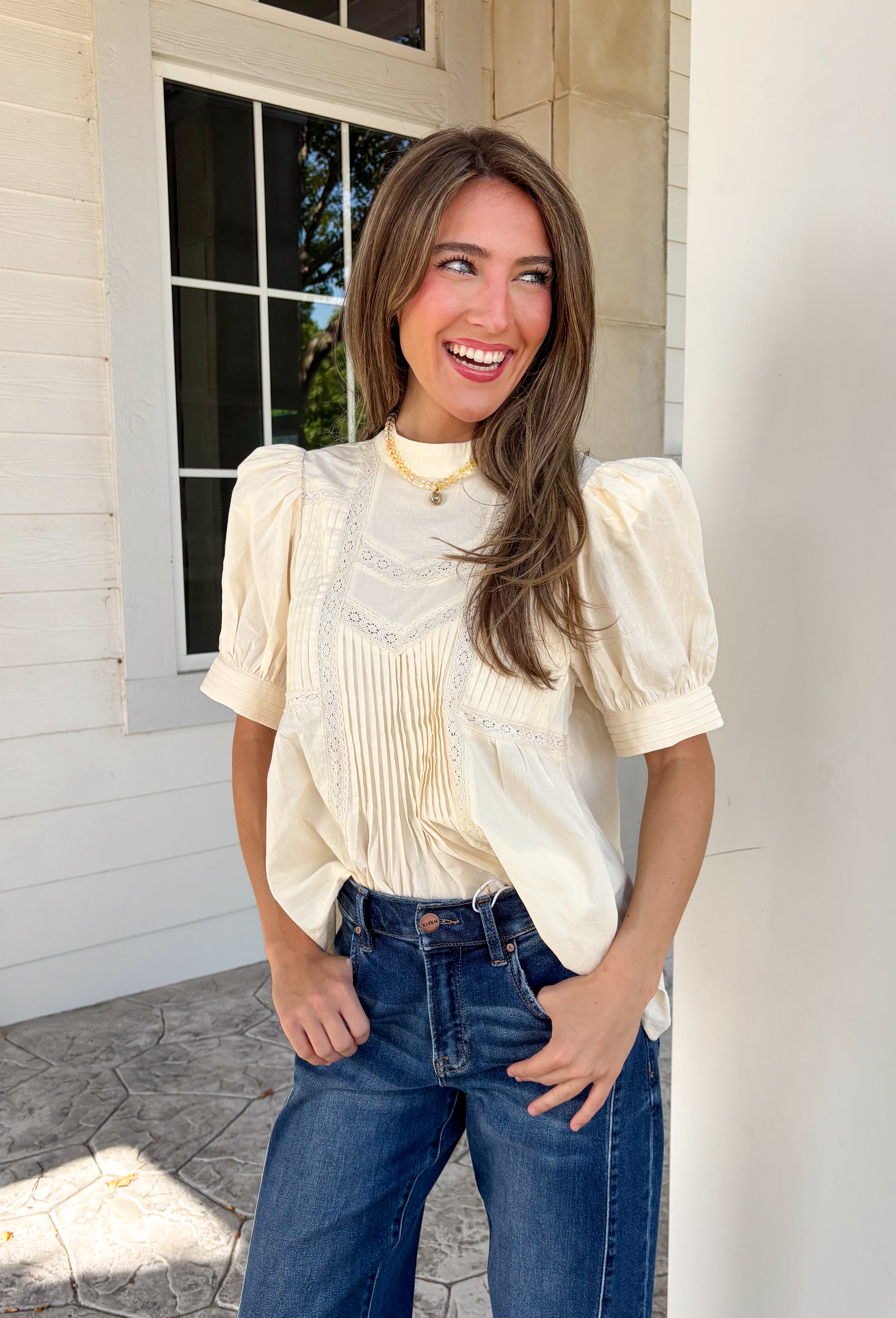 Soft, feminine, and effortlessly timeless, this beautiful ecru top is the kind of piece you'll treasure season after season! Crafted from breathable cotton, it features delicate lace detailing and chic pleating throughout for a look that's both romantic and refined. The puff sleeves add just the right amount of charm, while the keyhole button closure at the back provides a graceful finishing touch. 