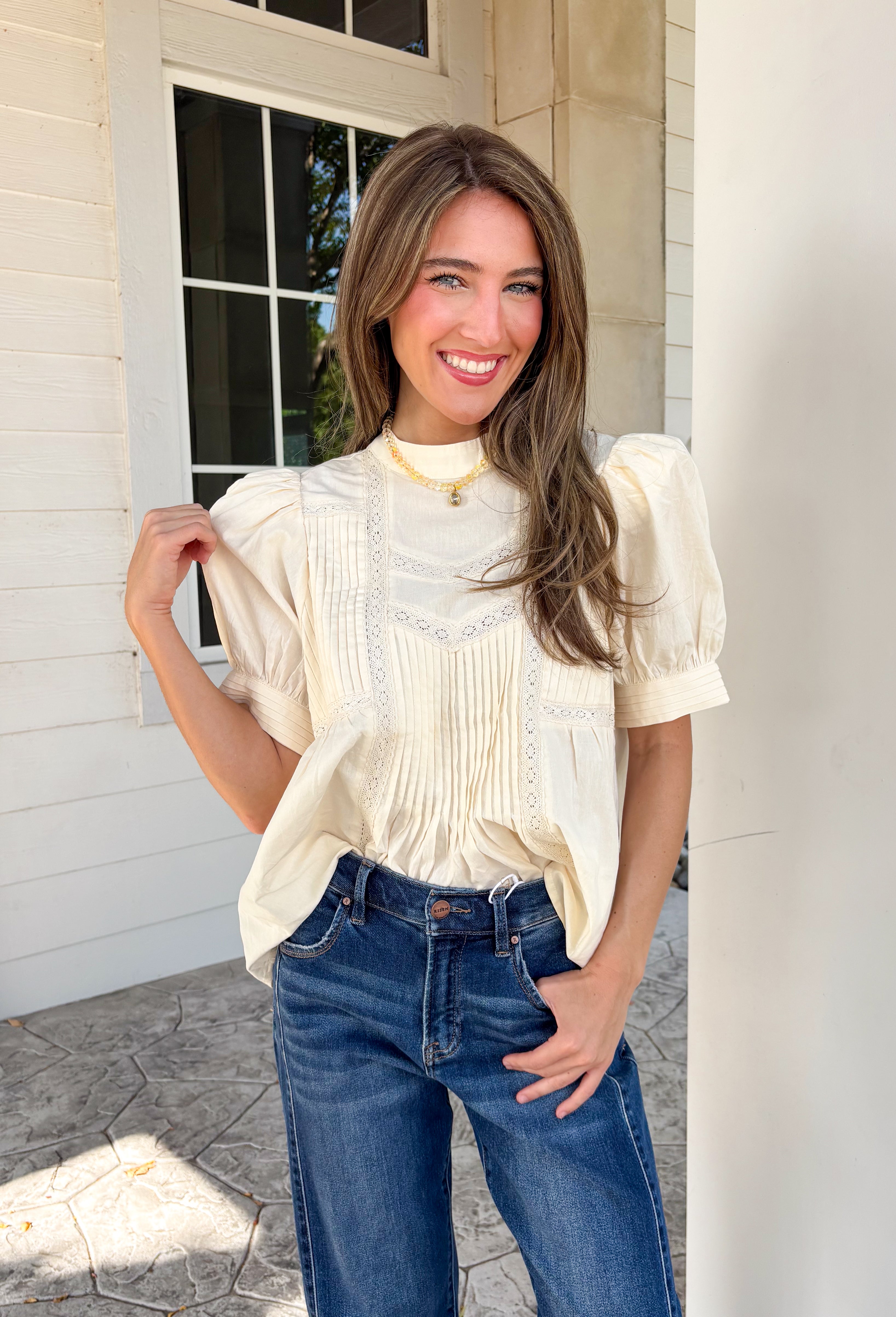 Soft, feminine, and effortlessly timeless, this beautiful ecru top is the kind of piece you'll treasure season after season! Crafted from breathable cotton, it features delicate lace detailing and chic pleating throughout for a look that's both romantic and refined. The puff sleeves add just the right amount of charm, while the keyhole button closure at the back provides a graceful finishing touch. 