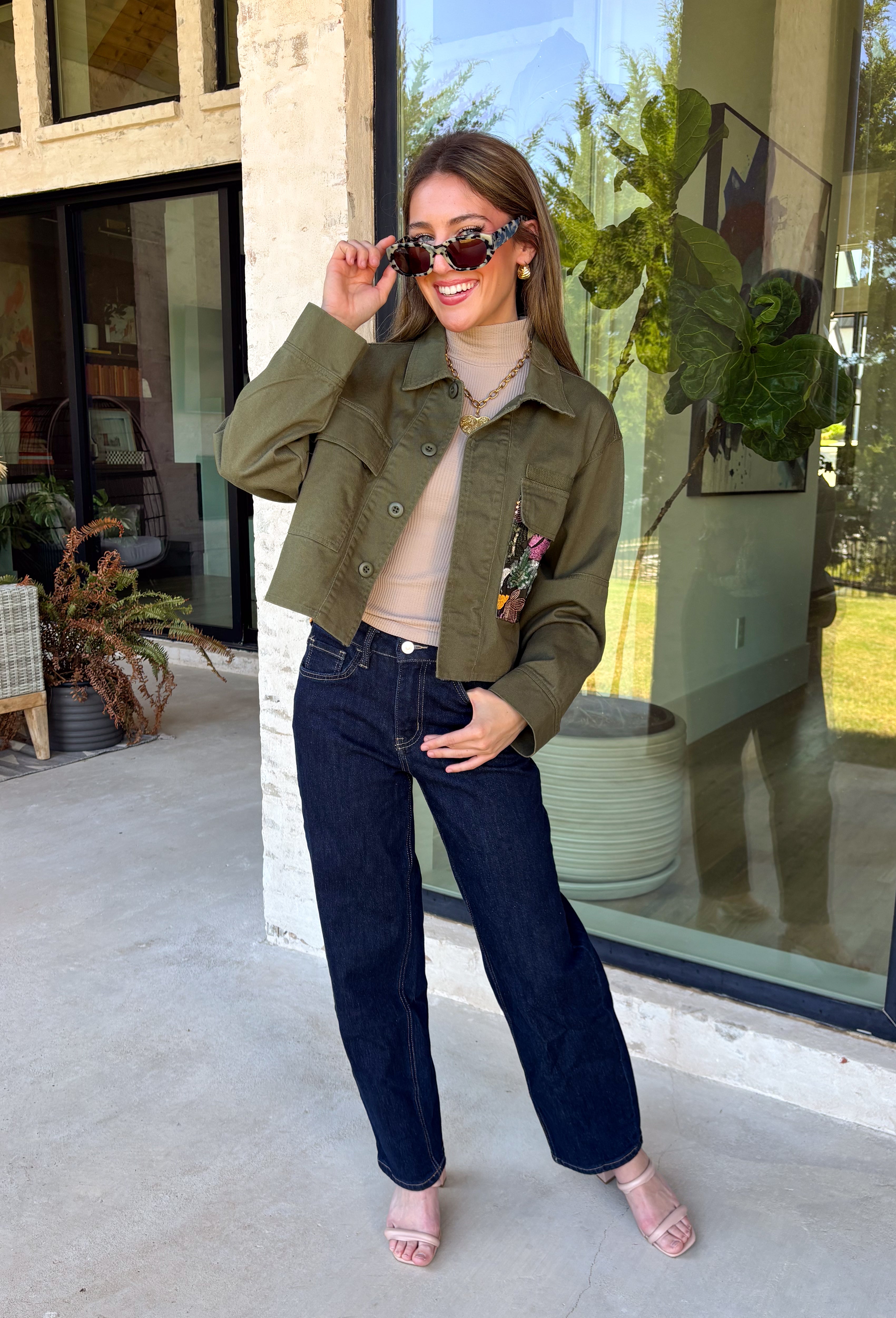 Make a statement everywhere you go with this stunning denim jacket from Veveret. Crafted in a rich olive denim, this standout layer features a breathtaking sheer embroidered floral design across the back, accented with shimmering sequins in shades of green, pink, orange, and brown. Coordinating floral sequin details on the front pockets tie the look together beautifully, while the classic collared neckline and button-front design keep it timeless. 