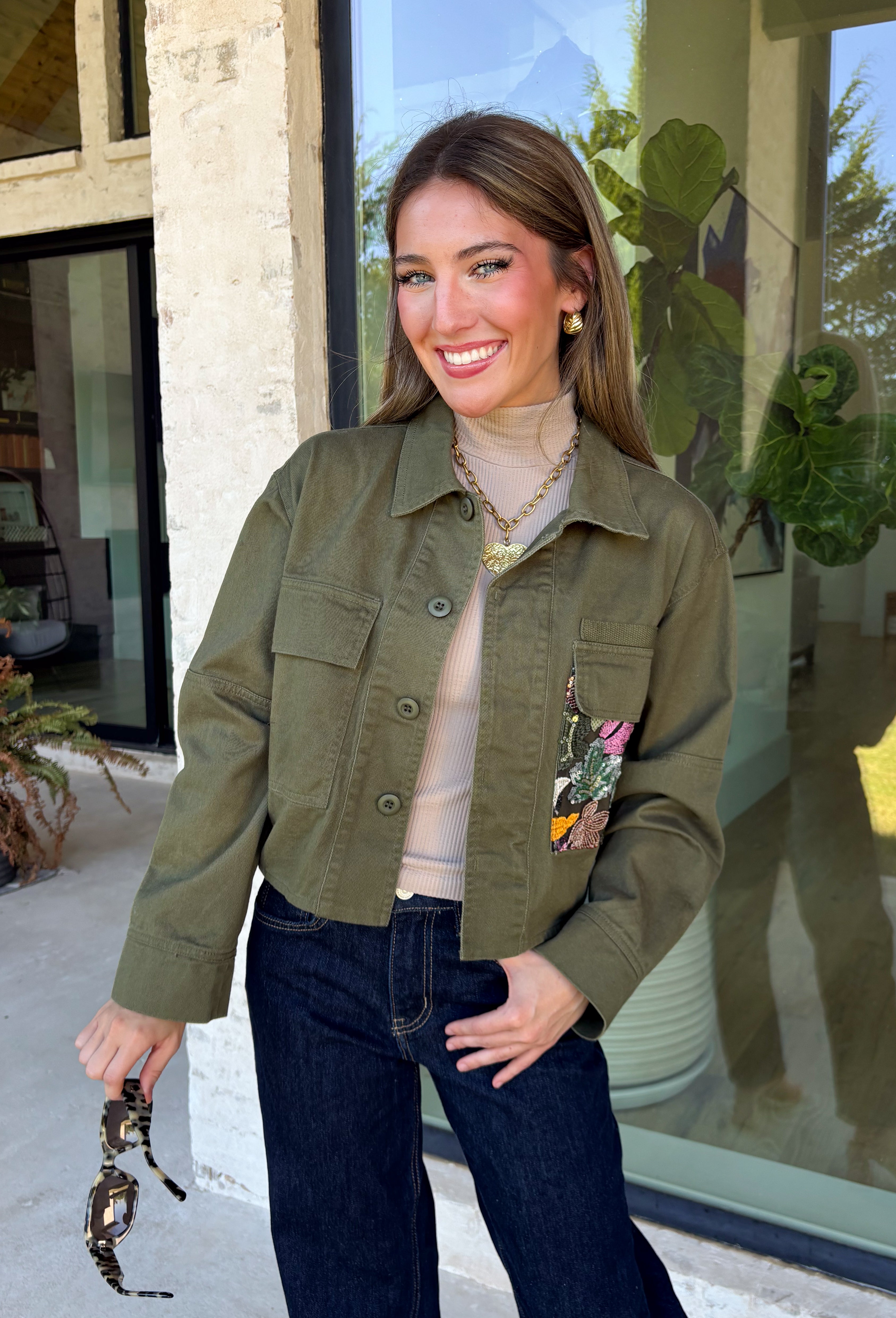 Make a statement everywhere you go with this stunning denim jacket from Veveret. Crafted in a rich olive denim, this standout layer features a breathtaking sheer embroidered floral design across the back, accented with shimmering sequins in shades of green, pink, orange, and brown. Coordinating floral sequin details on the front pockets tie the look together beautifully, while the classic collared neckline and button-front design keep it timeless. 