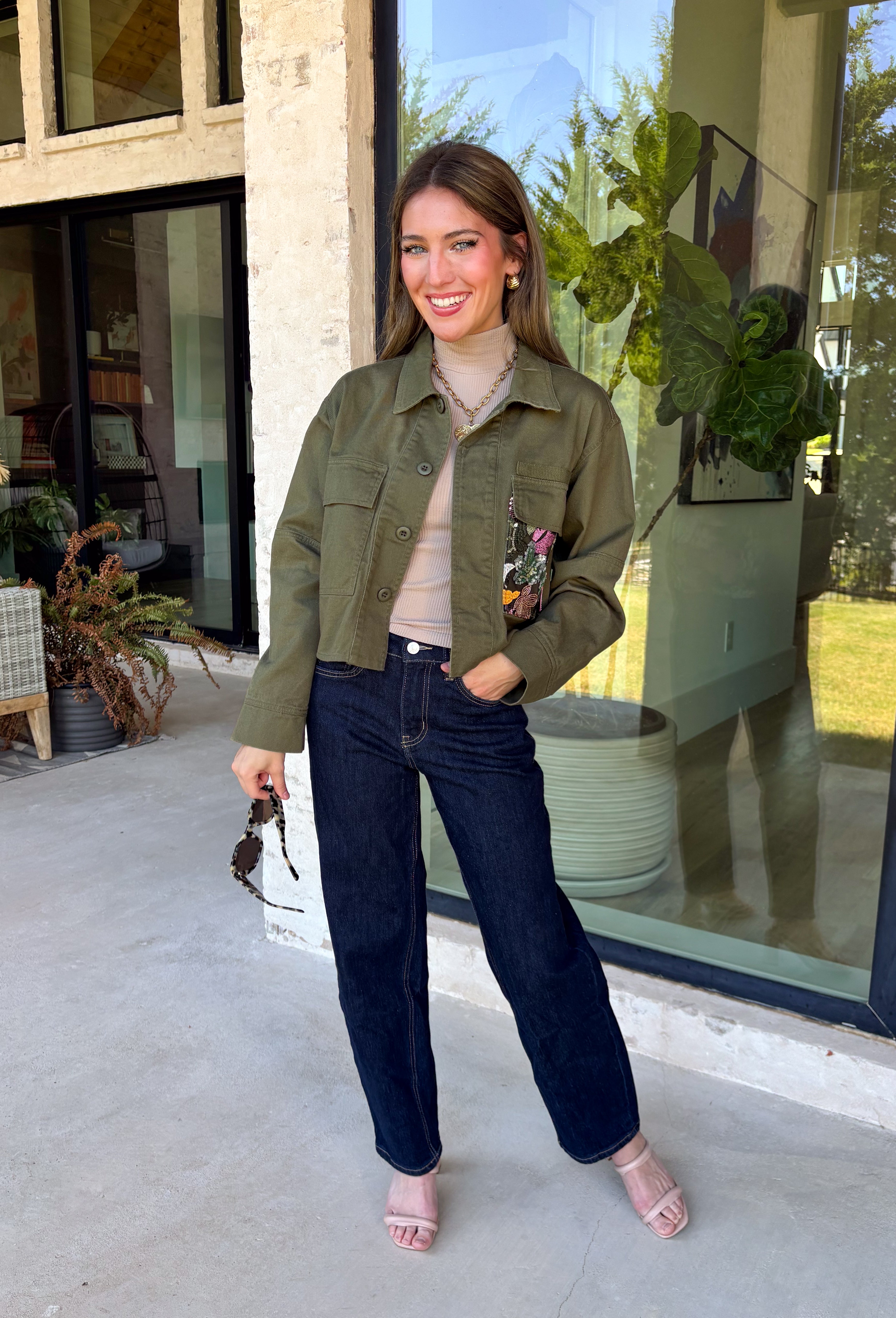 Make a statement everywhere you go with this stunning denim jacket from Veveret. Crafted in a rich olive denim, this standout layer features a breathtaking sheer embroidered floral design across the back, accented with shimmering sequins in shades of green, pink, orange, and brown. Coordinating floral sequin details on the front pockets tie the look together beautifully, while the classic collared neckline and button-front design keep it timeless. 