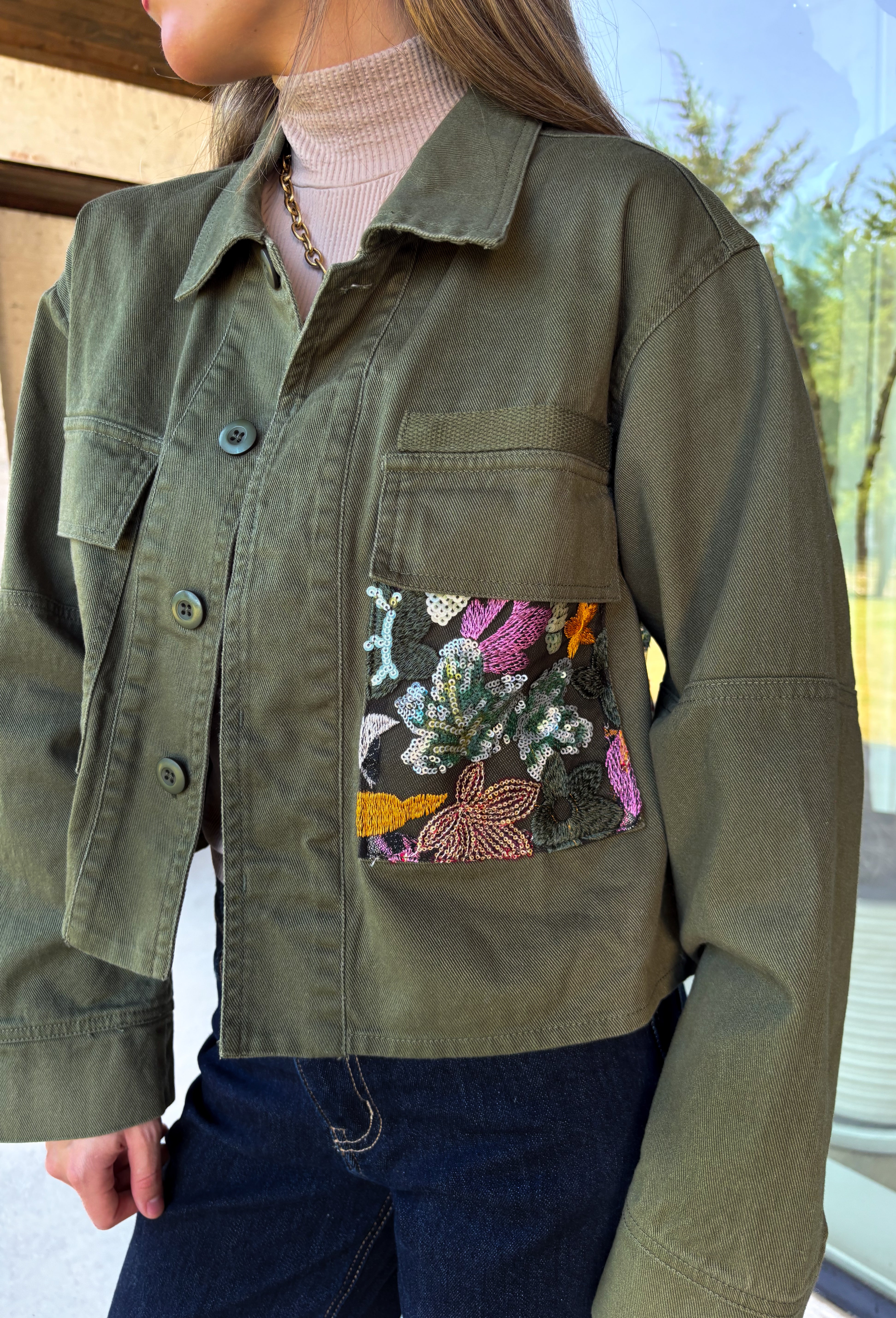 Make a statement everywhere you go with this stunning denim jacket from Veveret. Crafted in a rich olive denim, this standout layer features a breathtaking sheer embroidered floral design across the back, accented with shimmering sequins in shades of green, pink, orange, and brown. Coordinating floral sequin details on the front pockets tie the look together beautifully, while the classic collared neckline and button-front design keep it timeless. 