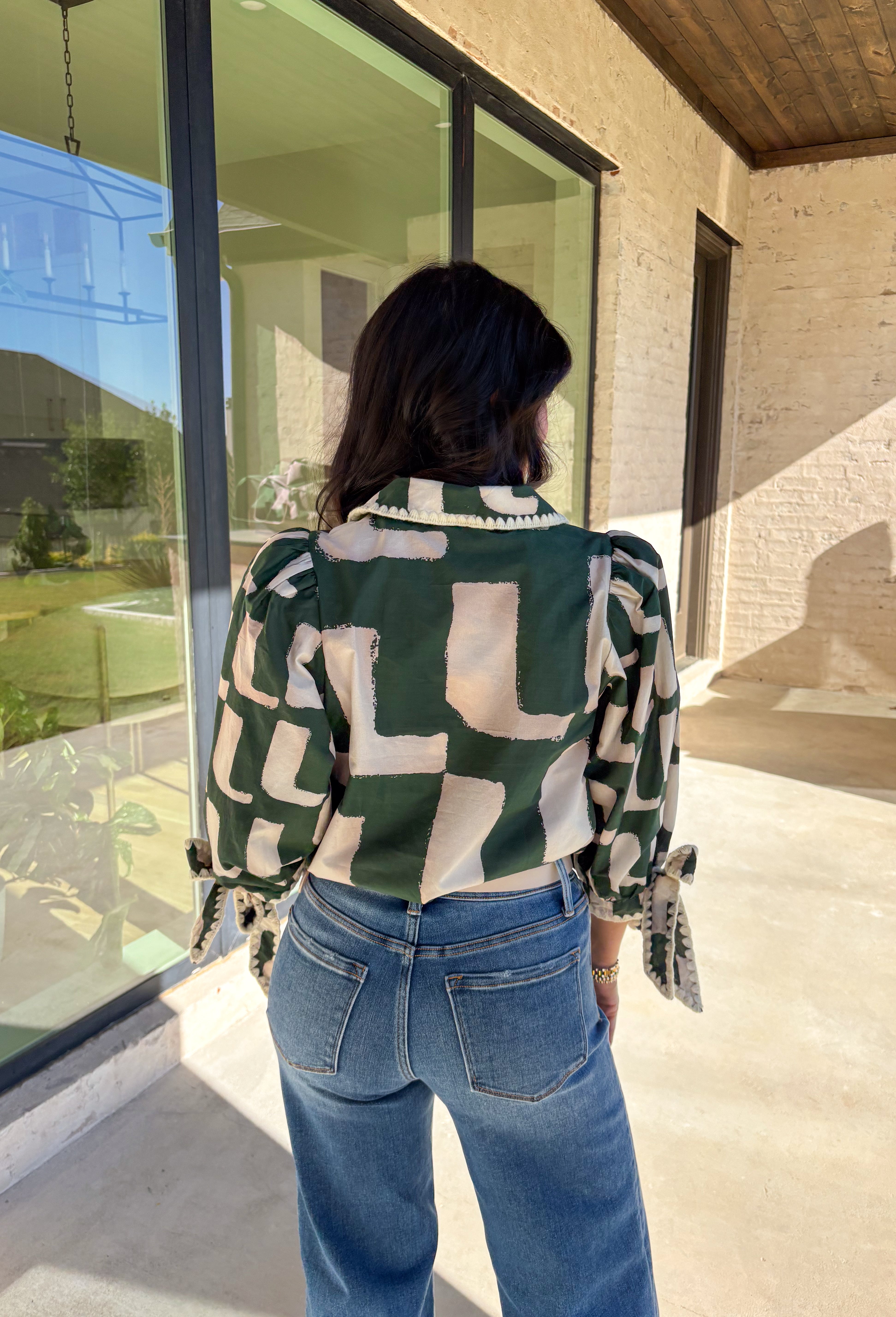 This hunter green top by Entro is full of personality and fall charm. Designed with an off-white abstract print, it features a split neckline with a collar and ¾ puff sleeves for a relaxed yet refined look. The scalloped trim and self-tie sleeve detail add a playful finish, giving this top a mix of polish and fun that’s easy to wear from workdays to weekends.