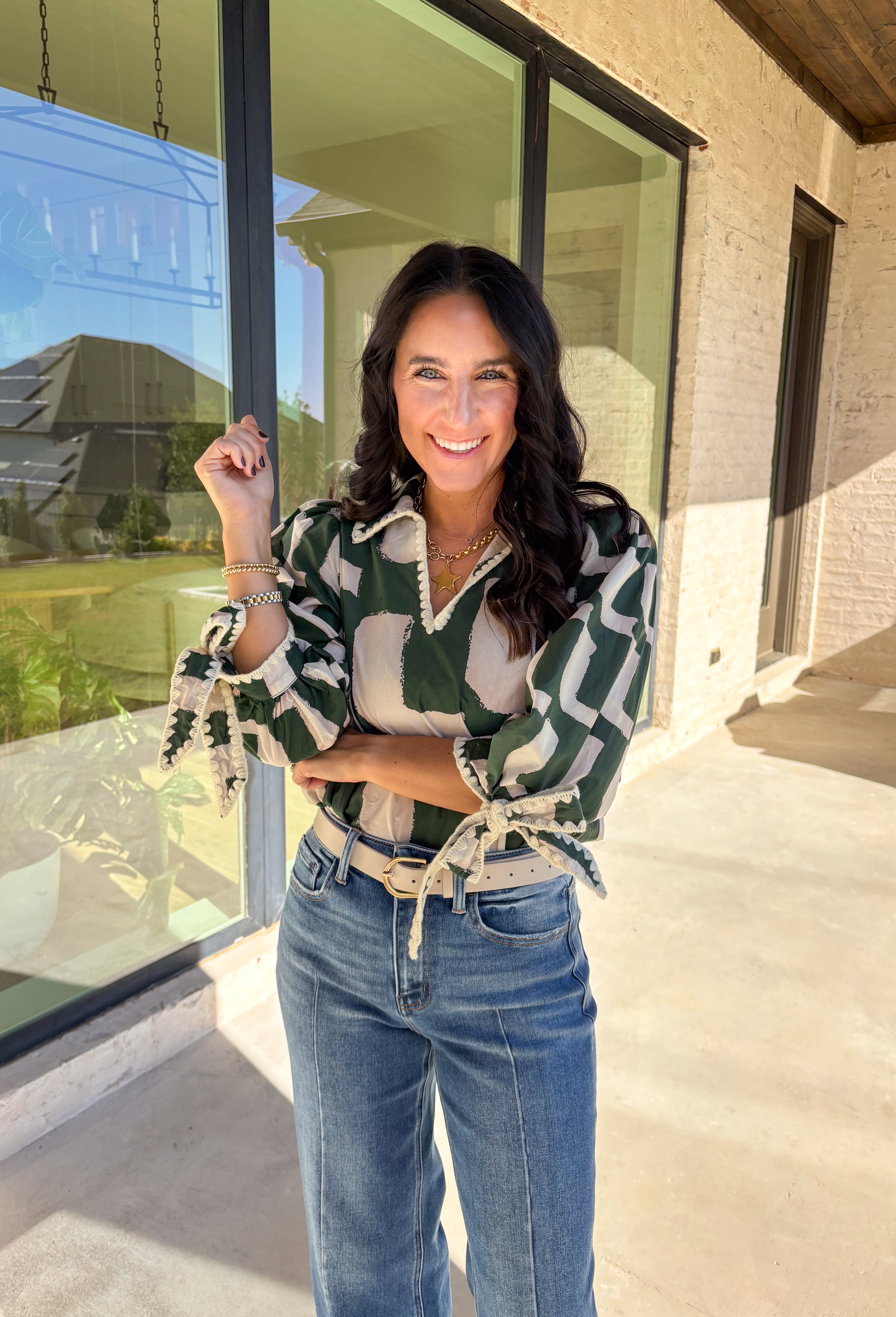 This hunter green top by Entro is full of personality and fall charm. Designed with an off-white abstract print, it features a split neckline with a collar and ¾ puff sleeves for a relaxed yet refined look. The scalloped trim and self-tie sleeve detail add a playful finish, giving this top a mix of polish and fun that’s easy to wear from workdays to weekends.