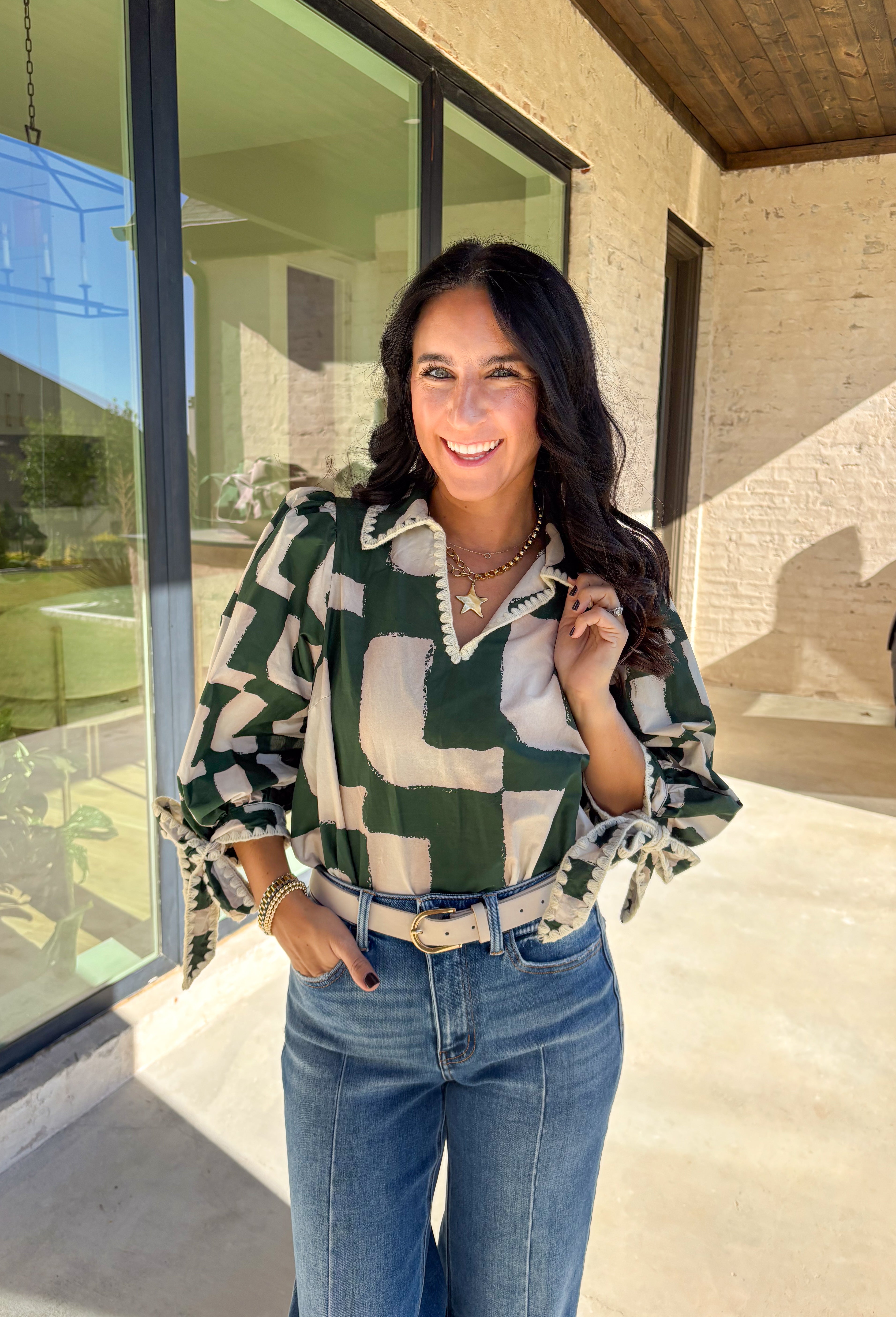 This hunter green top by Entro is full of personality and fall charm. Designed with an off-white abstract print, it features a split neckline with a collar and ¾ puff sleeves for a relaxed yet refined look. The scalloped trim and self-tie sleeve detail add a playful finish, giving this top a mix of polish and fun that’s easy to wear from workdays to weekends.