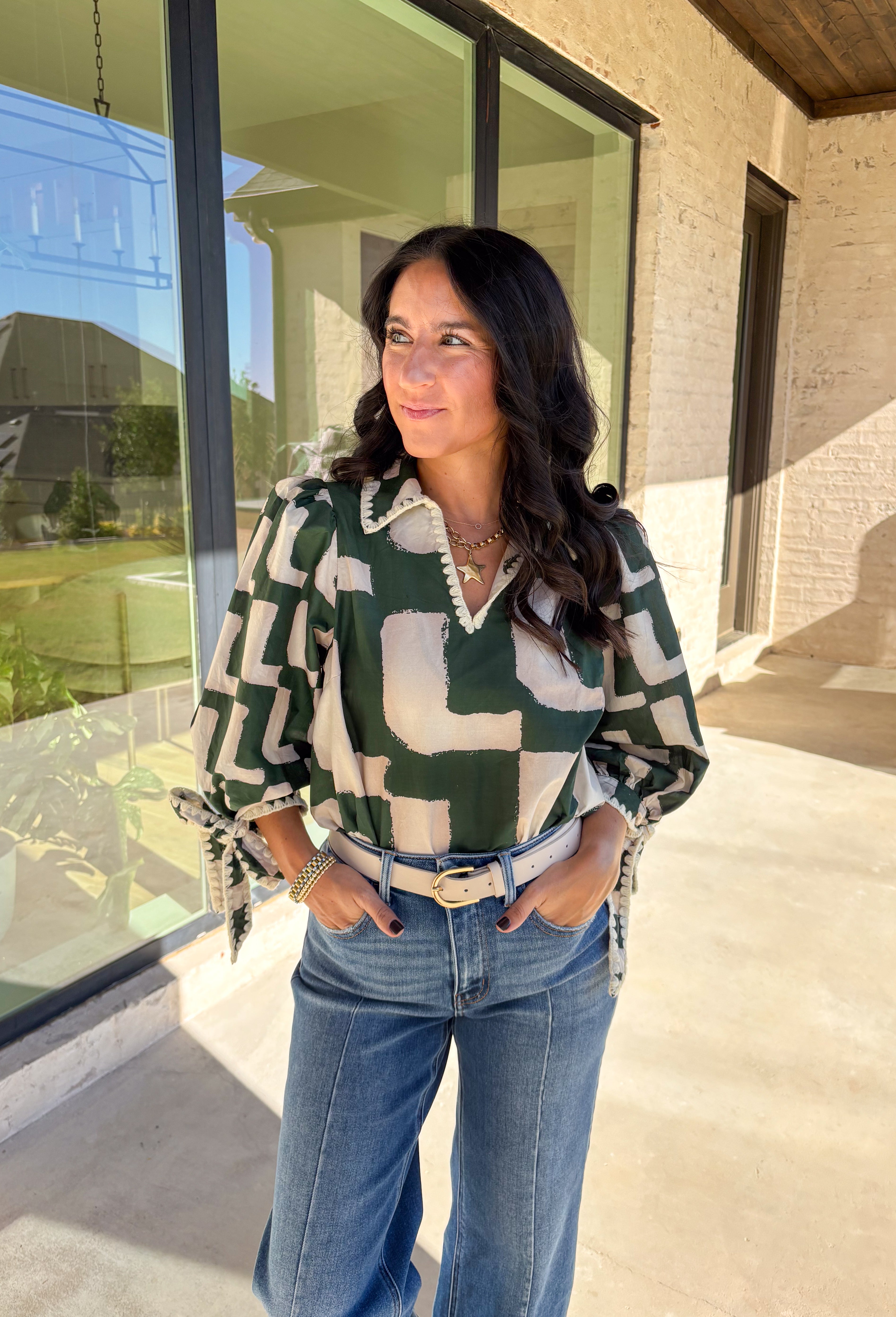 This hunter green top by Entro is full of personality and fall charm. Designed with an off-white abstract print, it features a split neckline with a collar and ¾ puff sleeves for a relaxed yet refined look. The scalloped trim and self-tie sleeve detail add a playful finish, giving this top a mix of polish and fun that’s easy to wear from workdays to weekends.